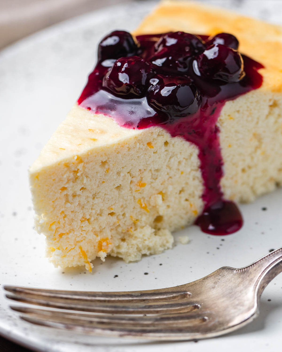 Closeup shot of Italian cheesecake with blueberry sauce on white plate.