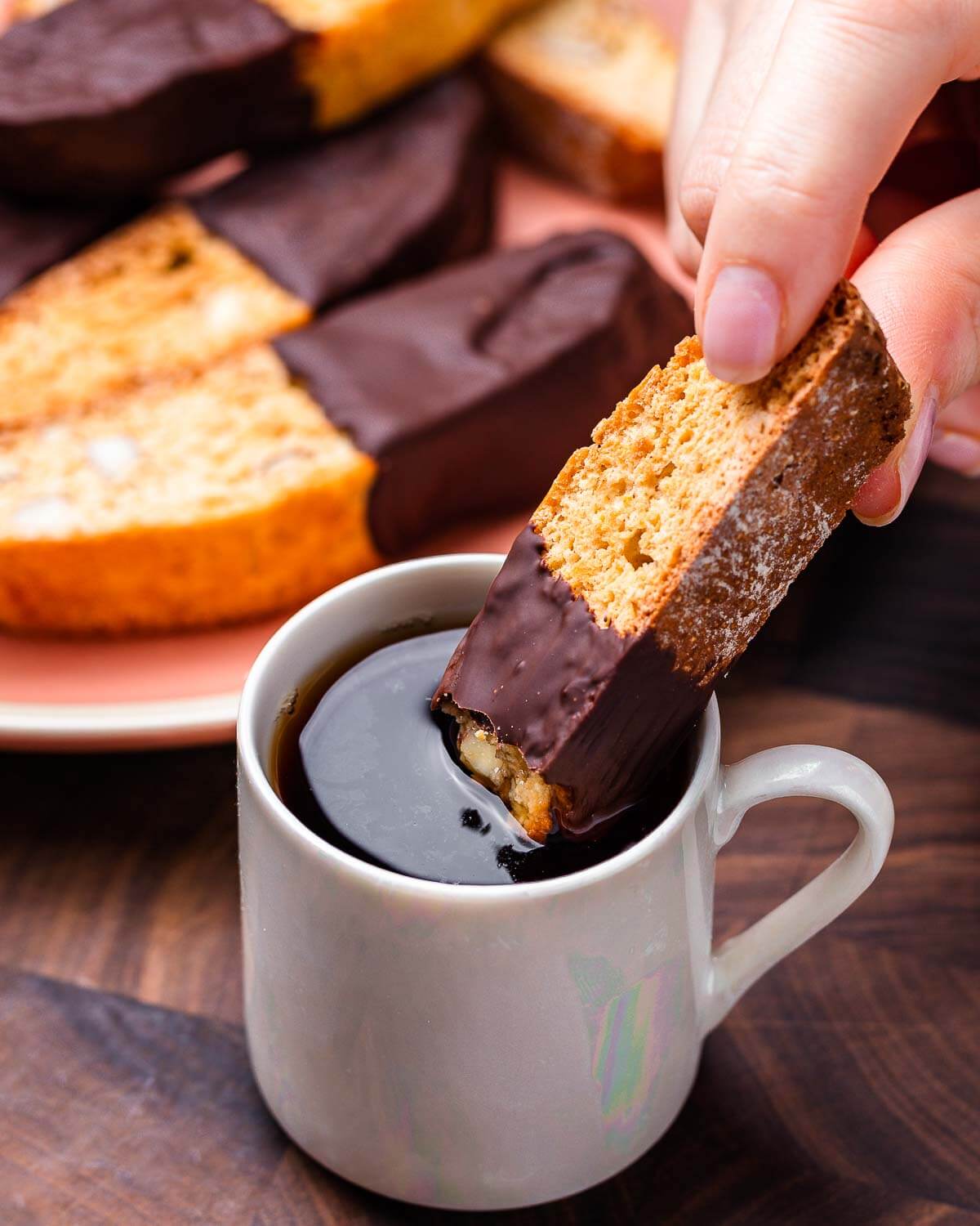 Hand dipping almond biscotti into coffee.