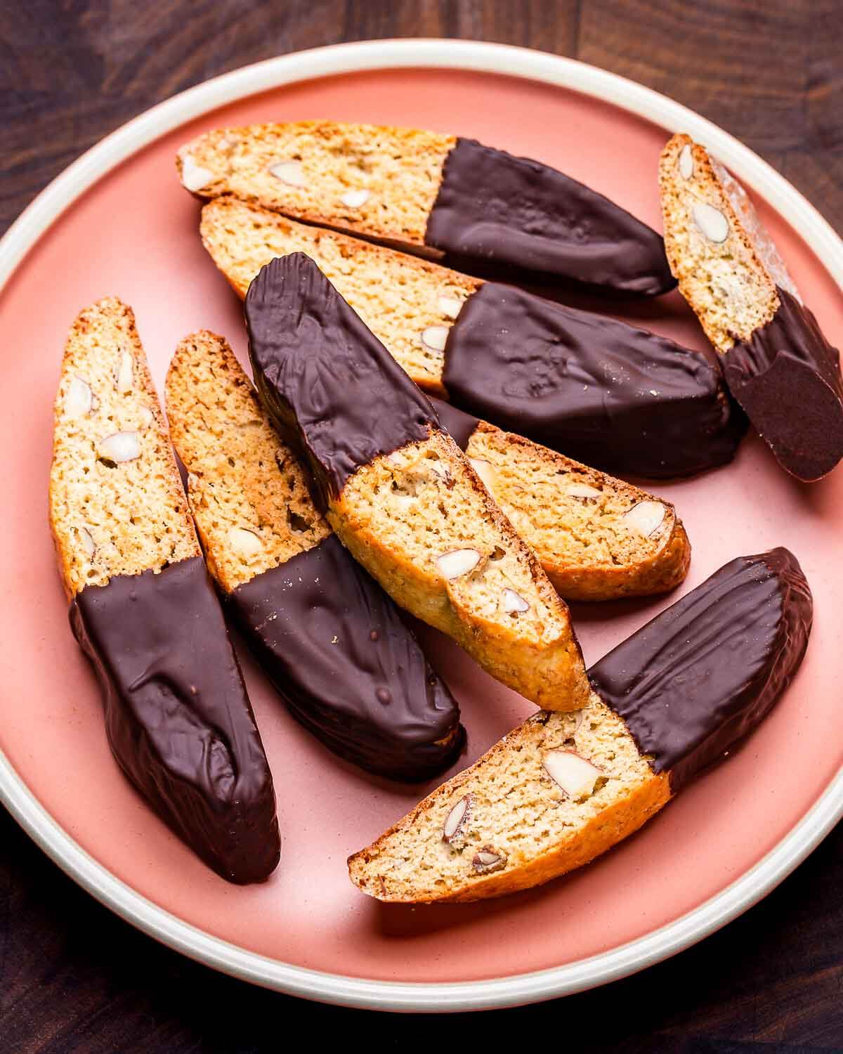 Almond biscotti with chocolate in pink plate on walnut cutting board.