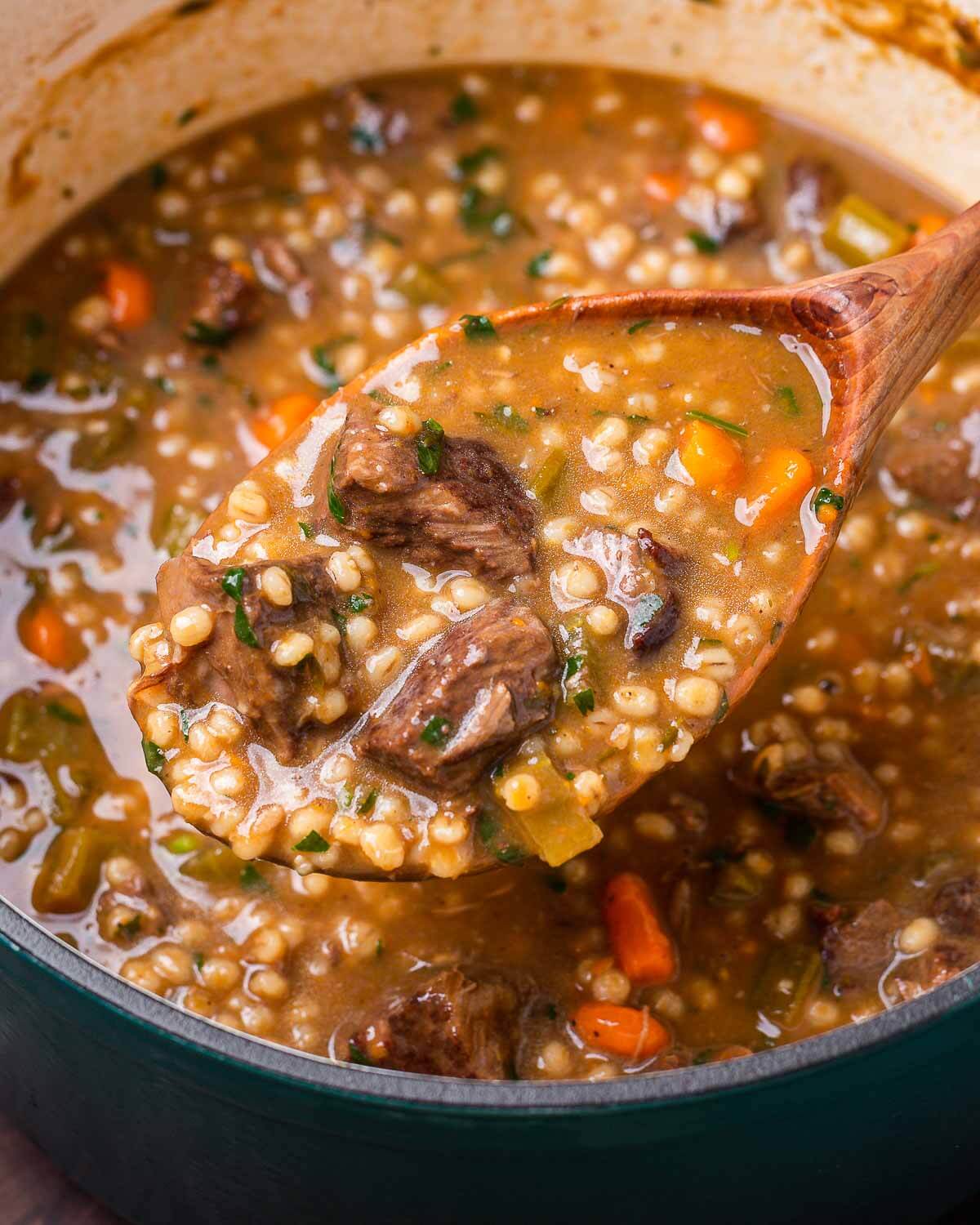 Large wooden ladle with beef barley soup over Dutch oven pot.