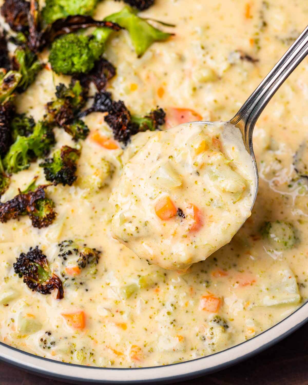 Spoonful of broccoli cheddar soup with roasted broccoli in the background.