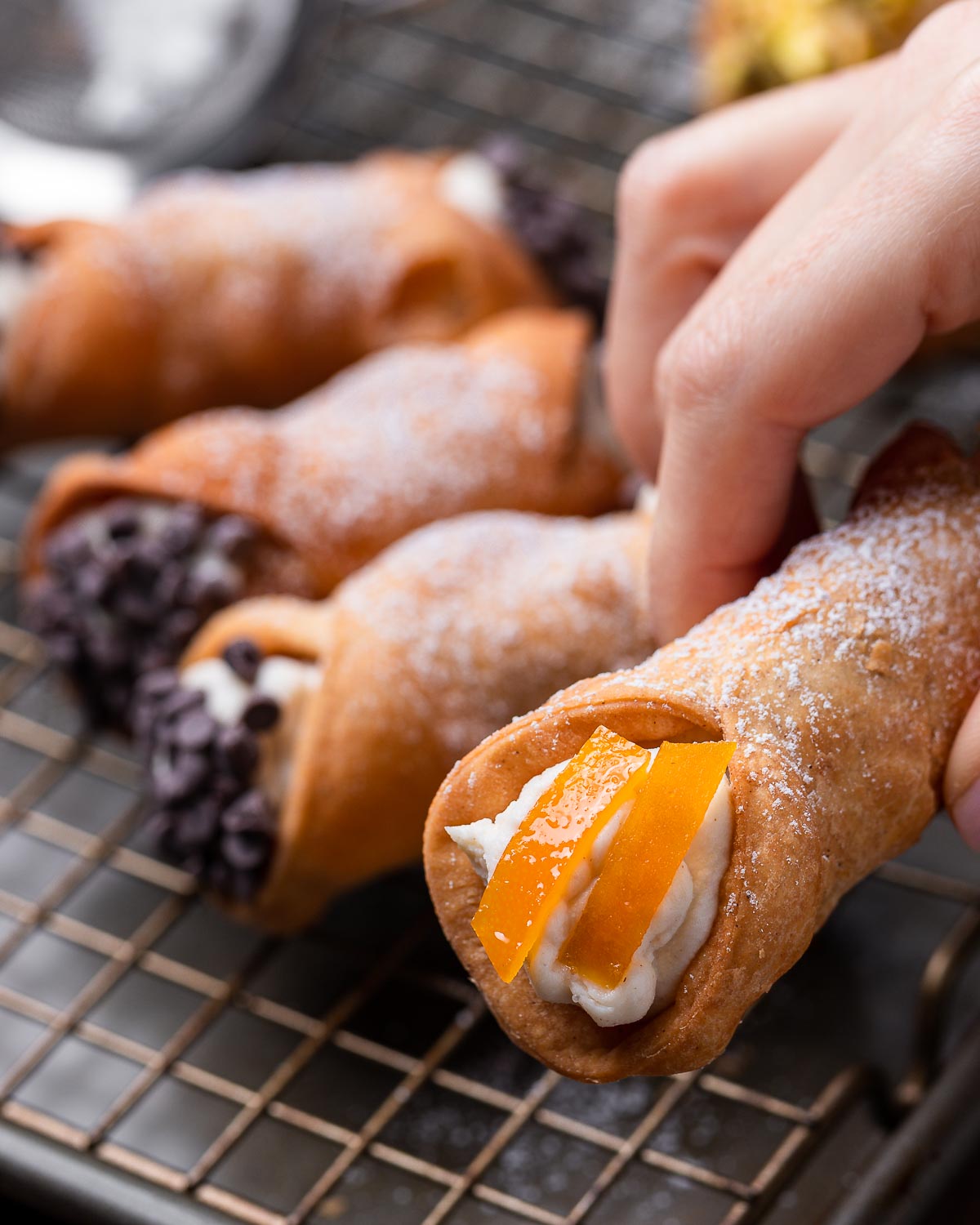 Hand holding a cannoli with candied orange peel.