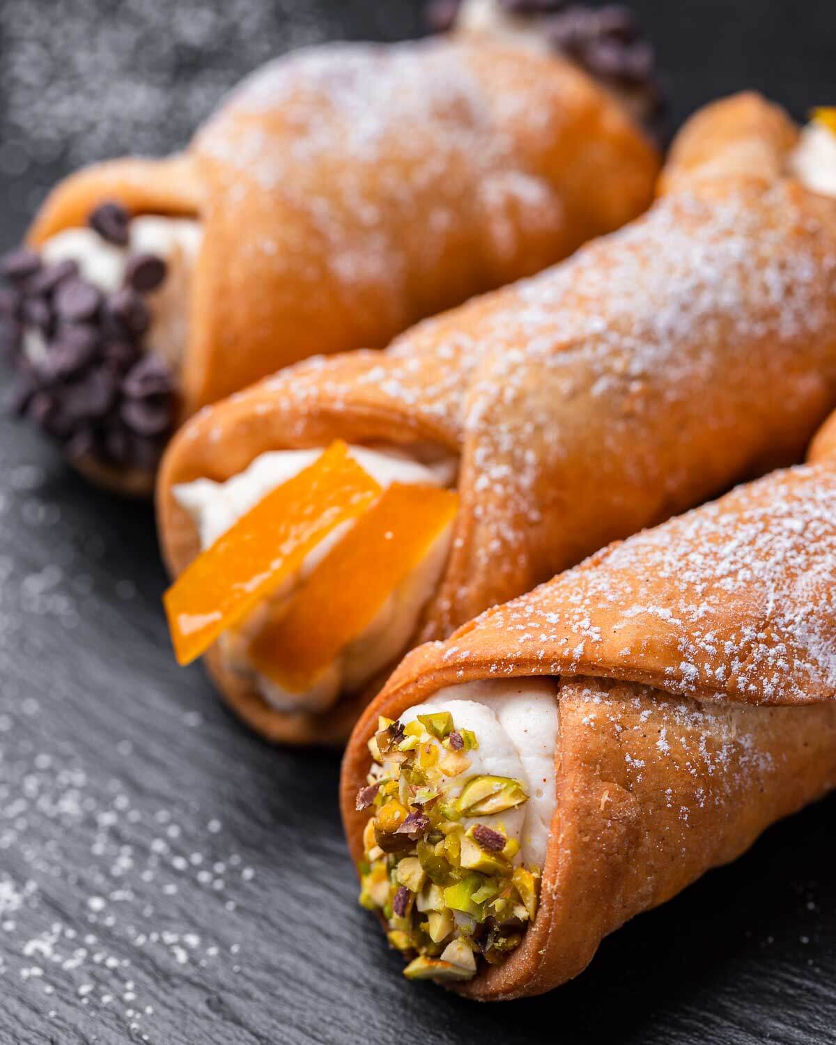 Cannoli with chocolate chips, candied orange, and pistachio on black slate.