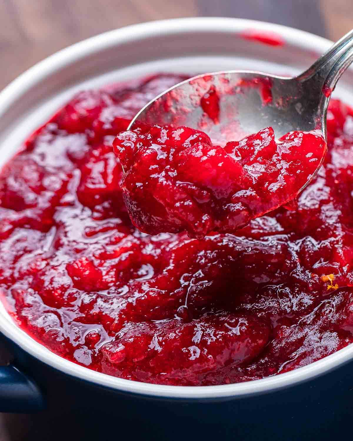 Spoonful of cranberry sauce over blue bowl.