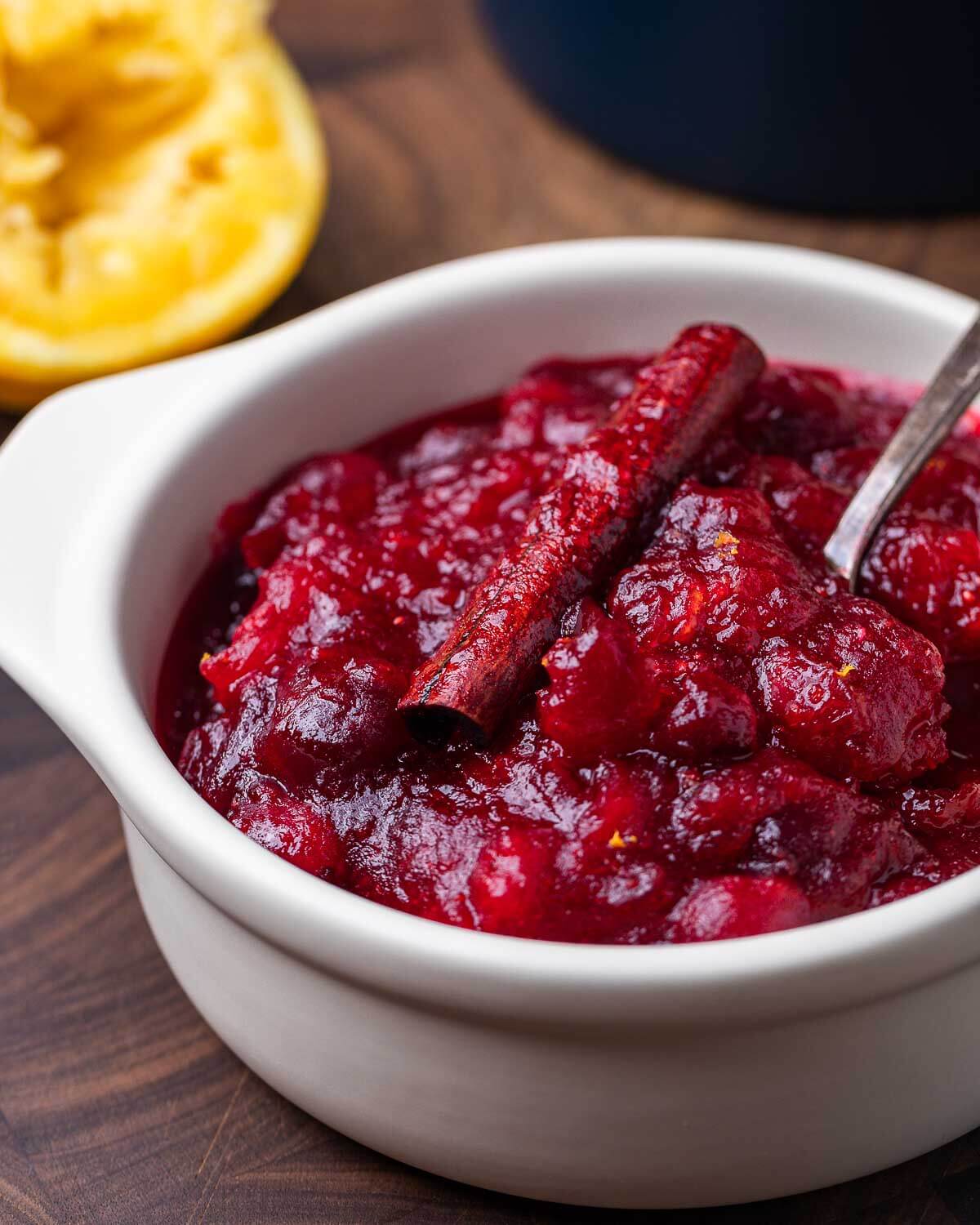 Cranberry sauce in white bowl with squeezed orange in background.
