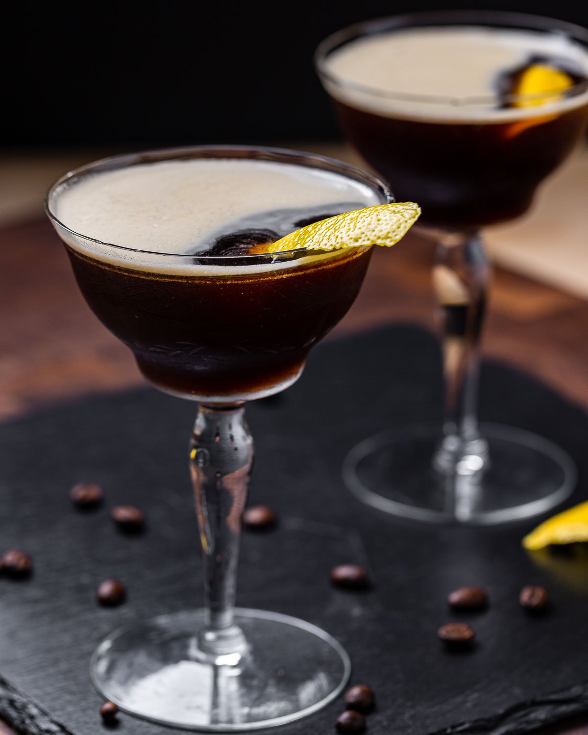 Two espresso martinis on black slate tile.