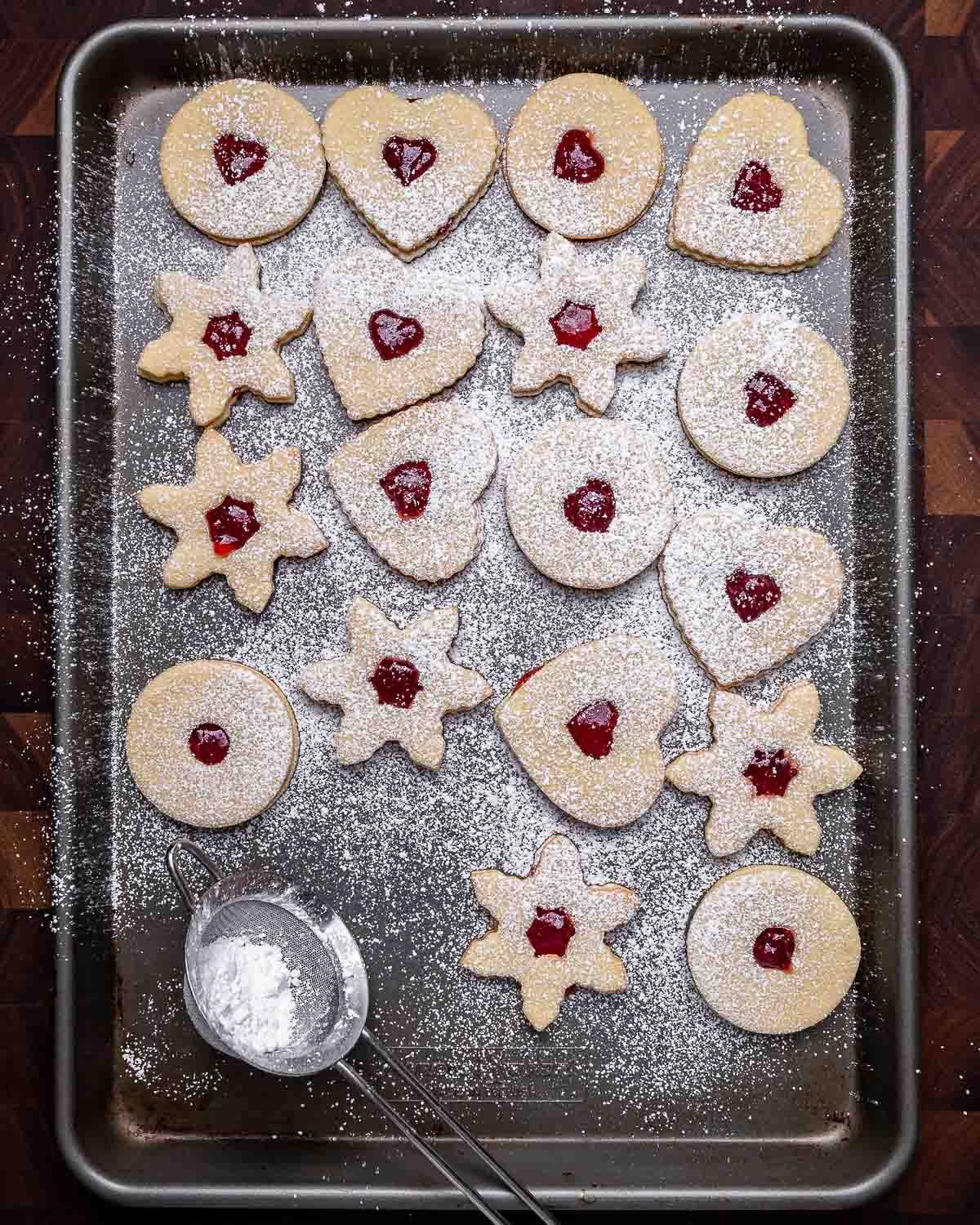 Overhead shot of linzer cookies with powdered sugar sifter on grey baking sheet.