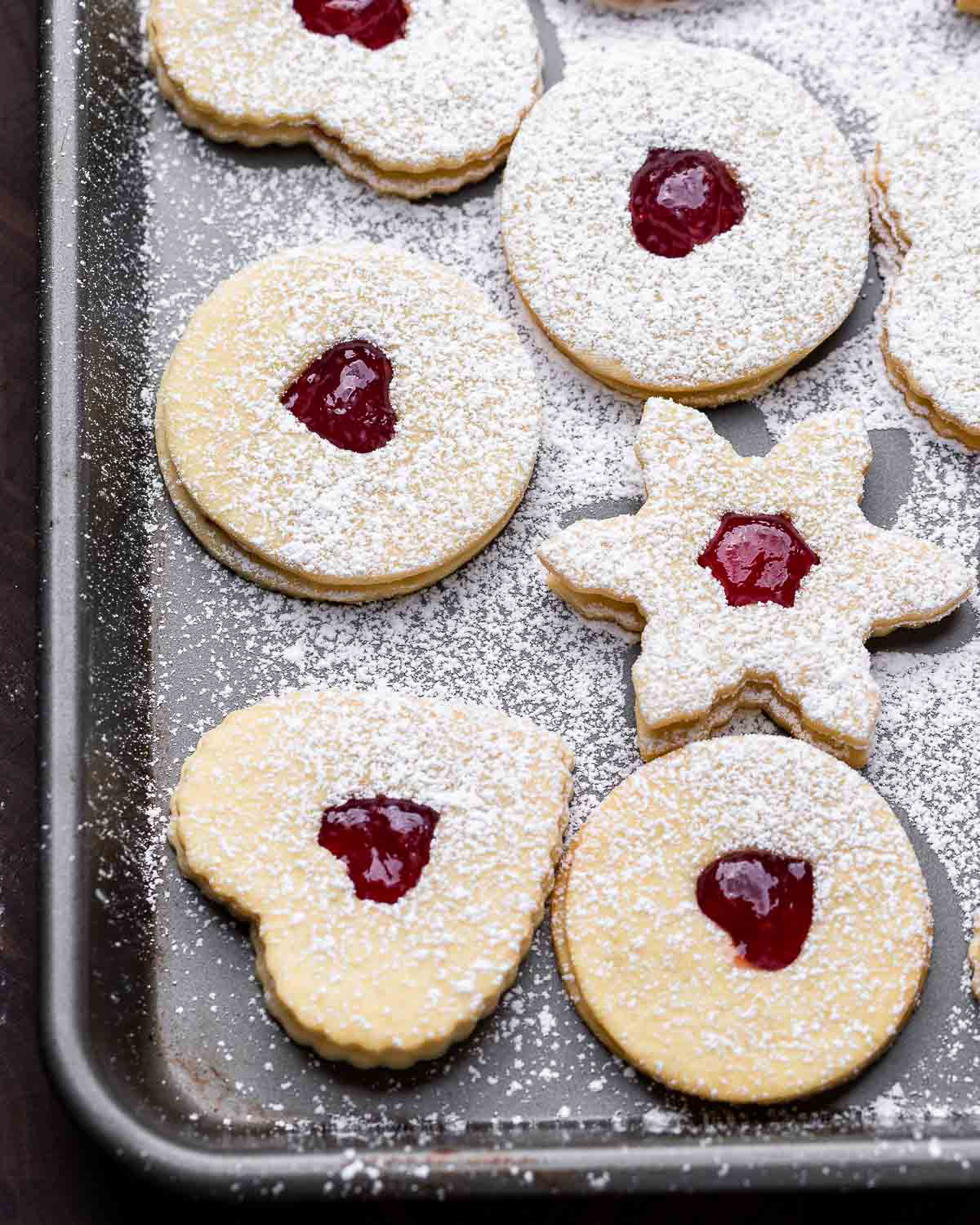 Overhead shot of linzer cookies with powdered sugar on grey baking sheet.