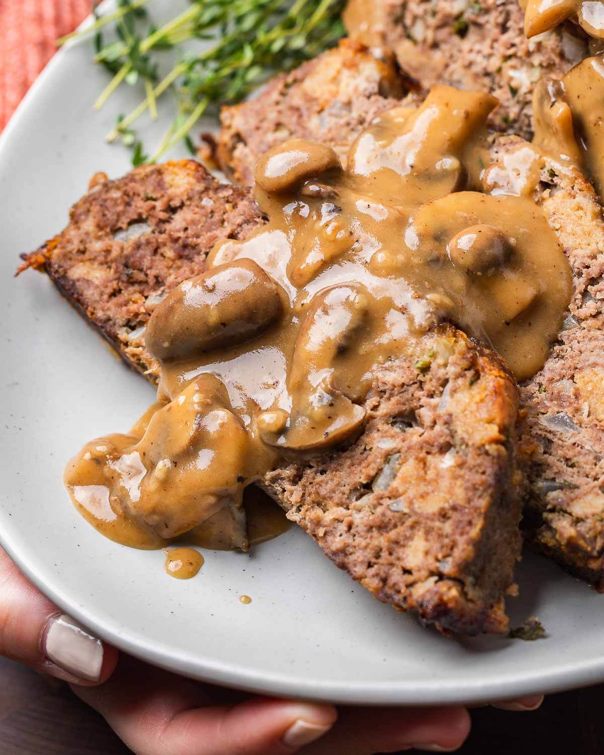 Hands holding platter of meatloaf with mushroom brown gravy.