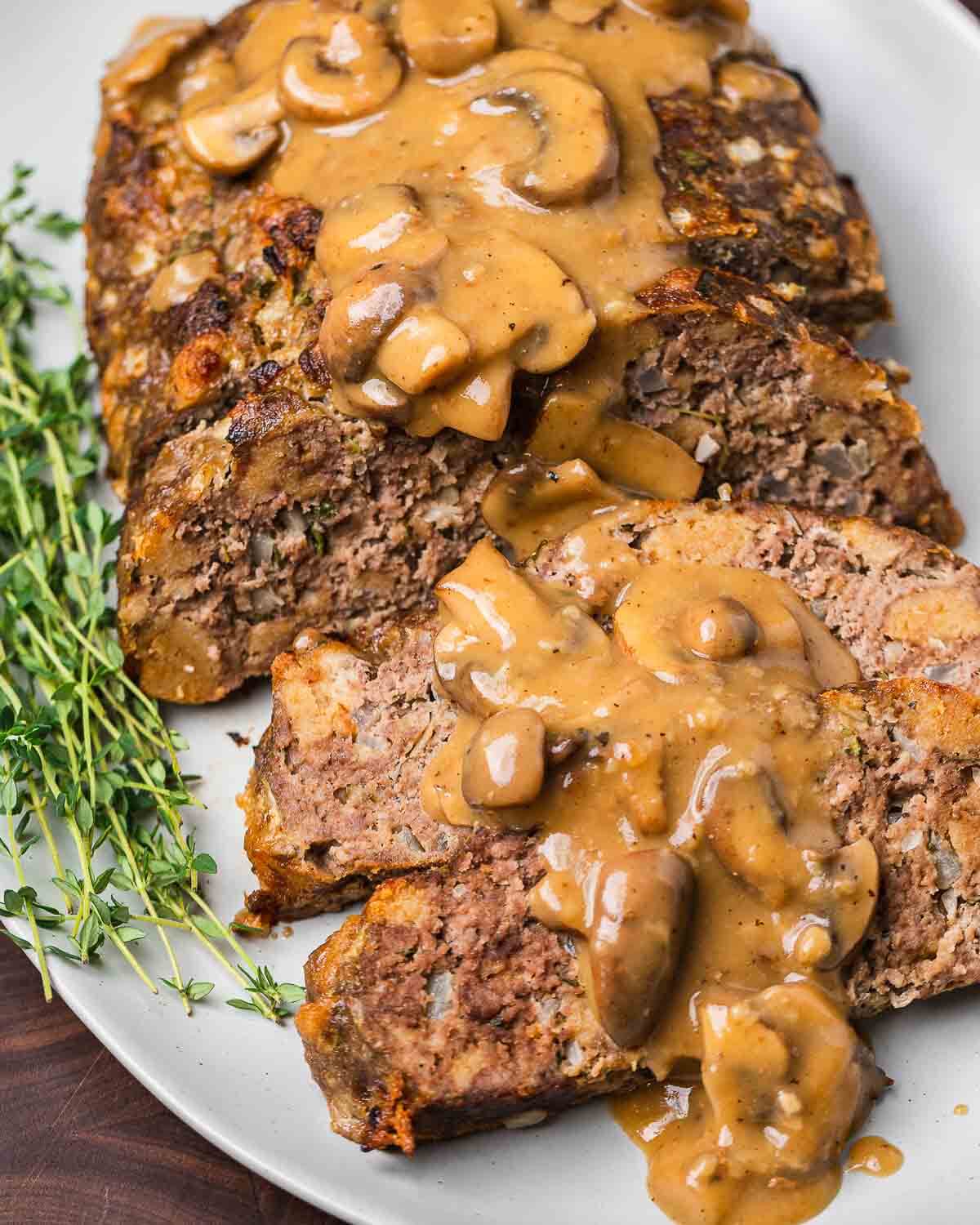 Slices of meatloaf with mushroom brown gravy in white platter.