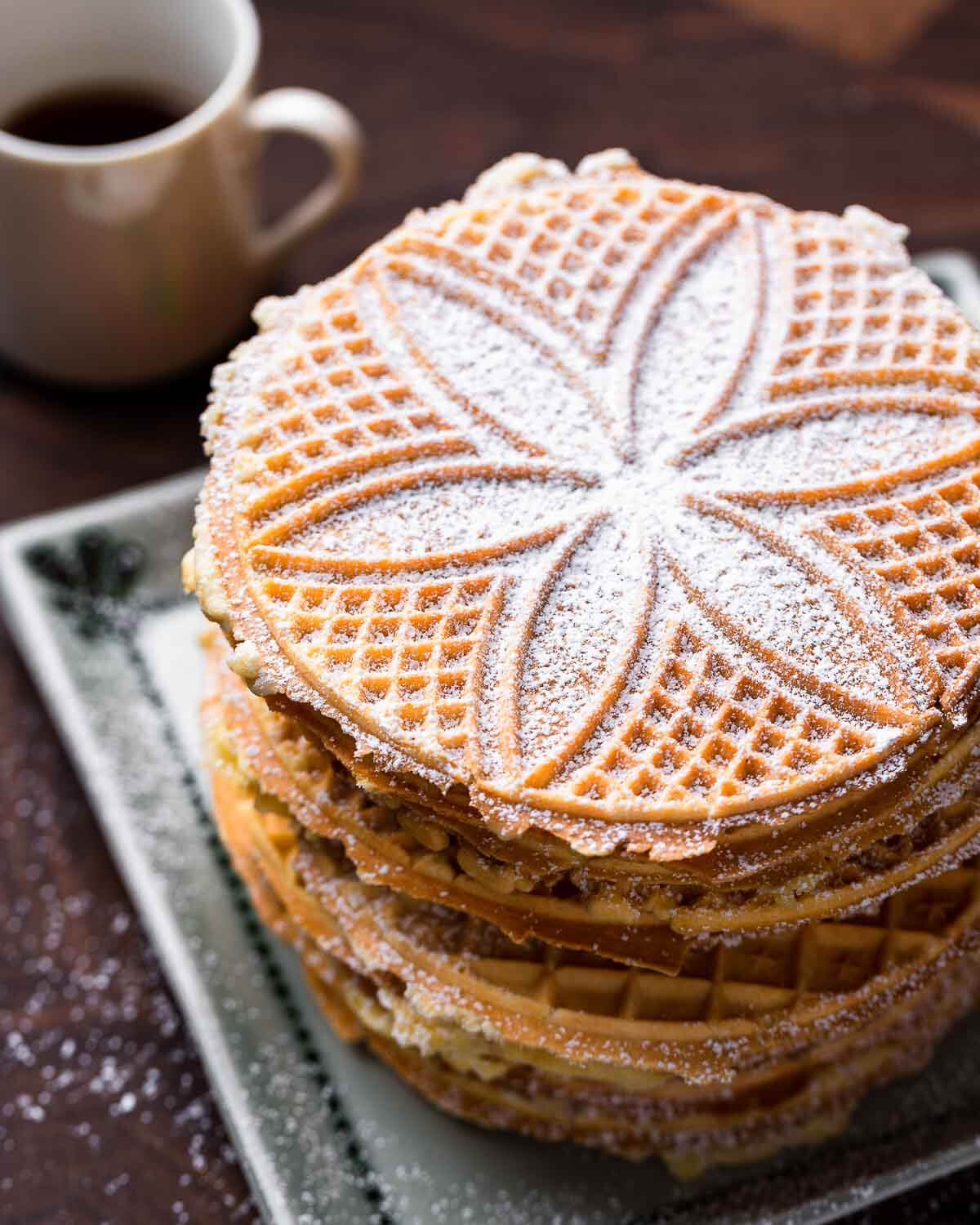 Stack of pizzelles with coffee mug in background.