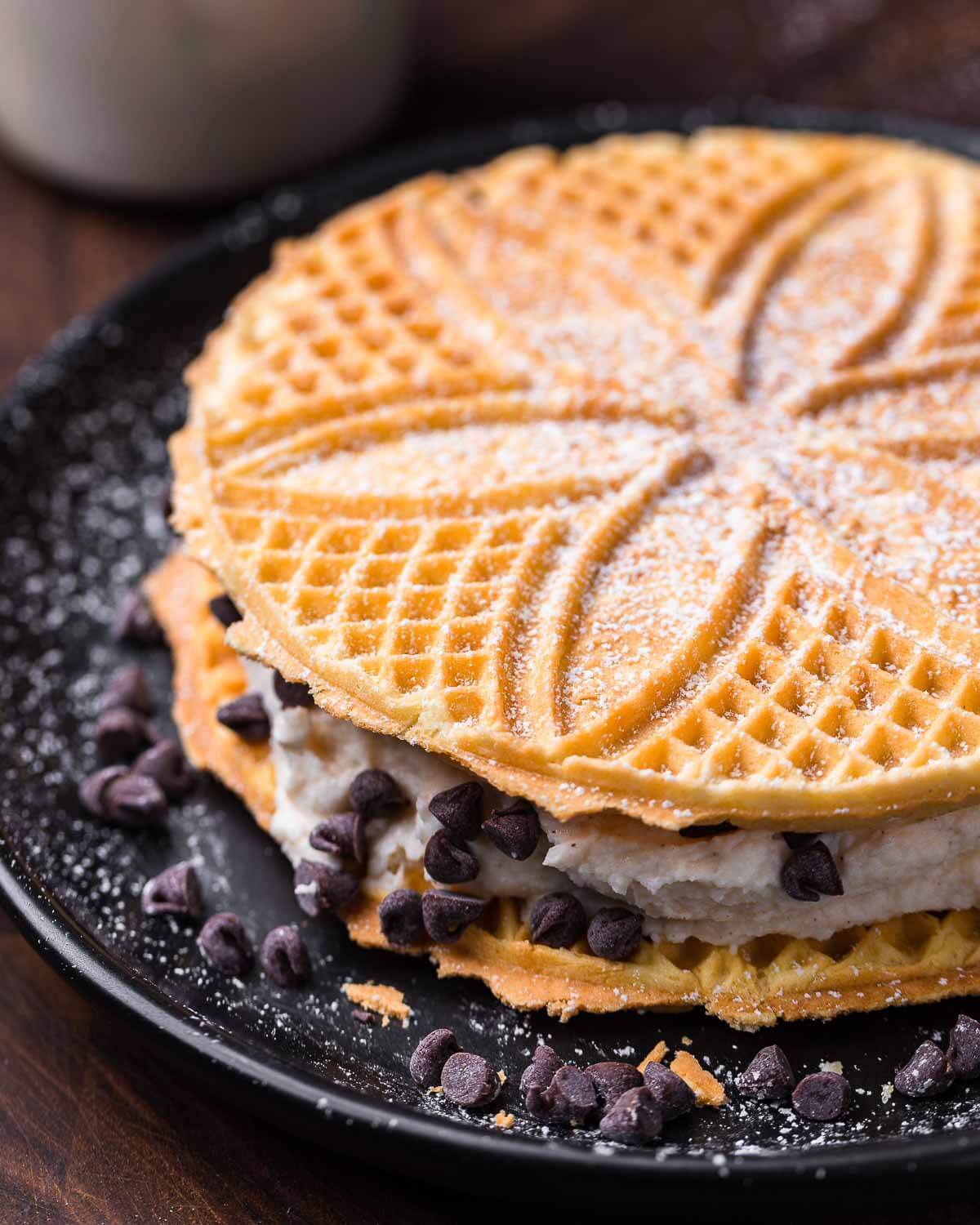 Pizzelle sandwich with cannoli cream on black plate.