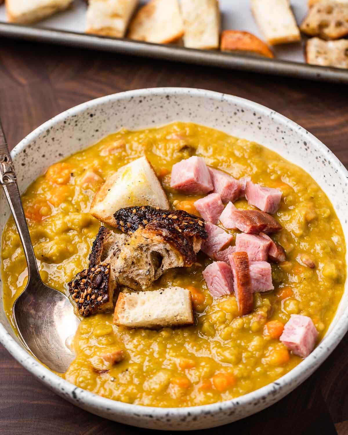 White bowl of split pea soup and tray of croutons in background.