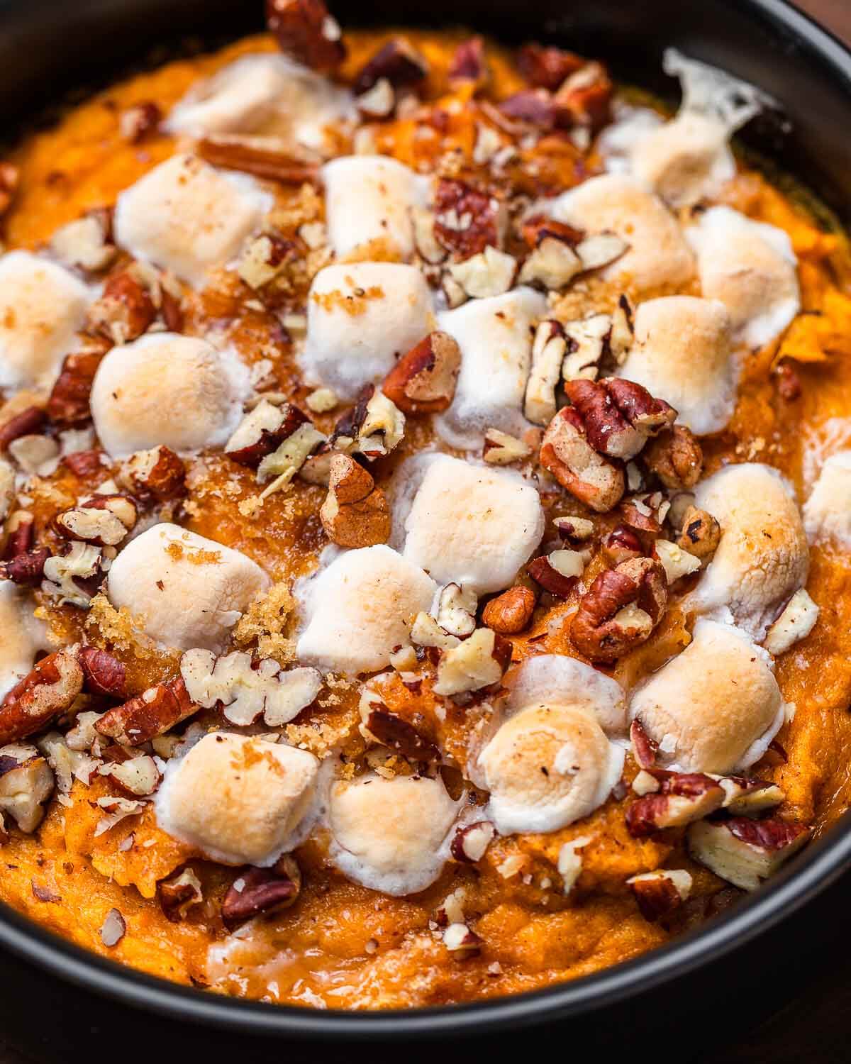 Sweet potato casserole with marshmallows and pecans in black bowl.