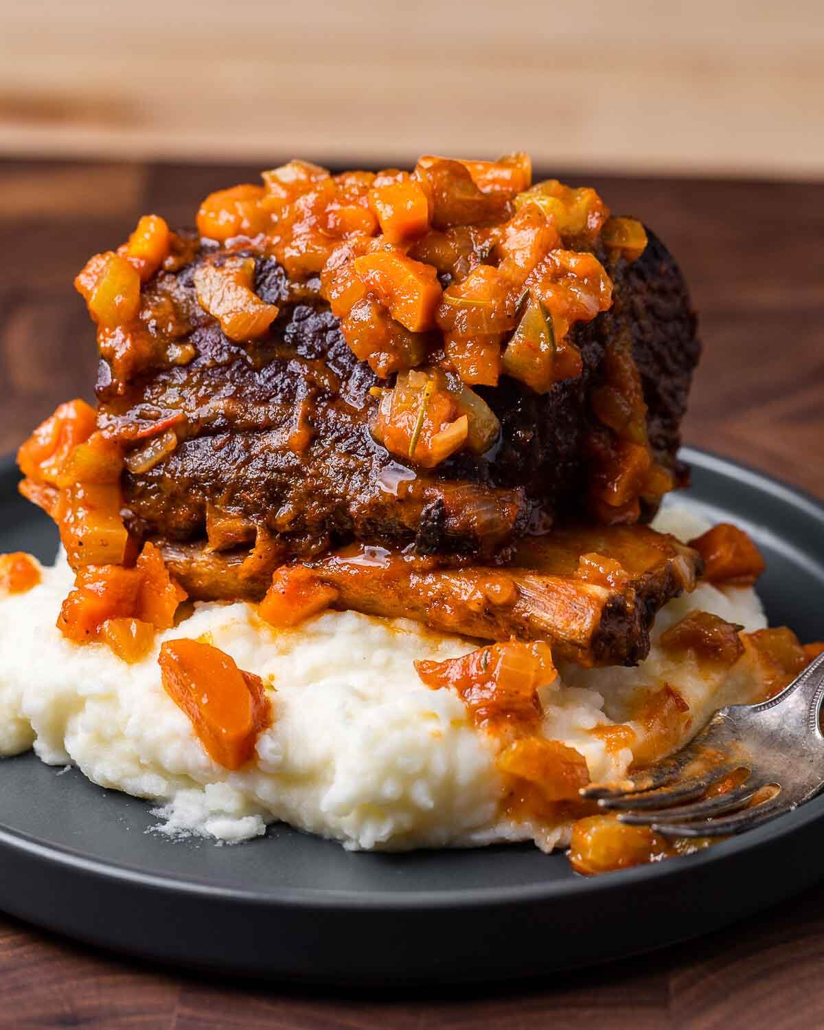 Large braised short rib on top of mashed potatoes in grey plate.