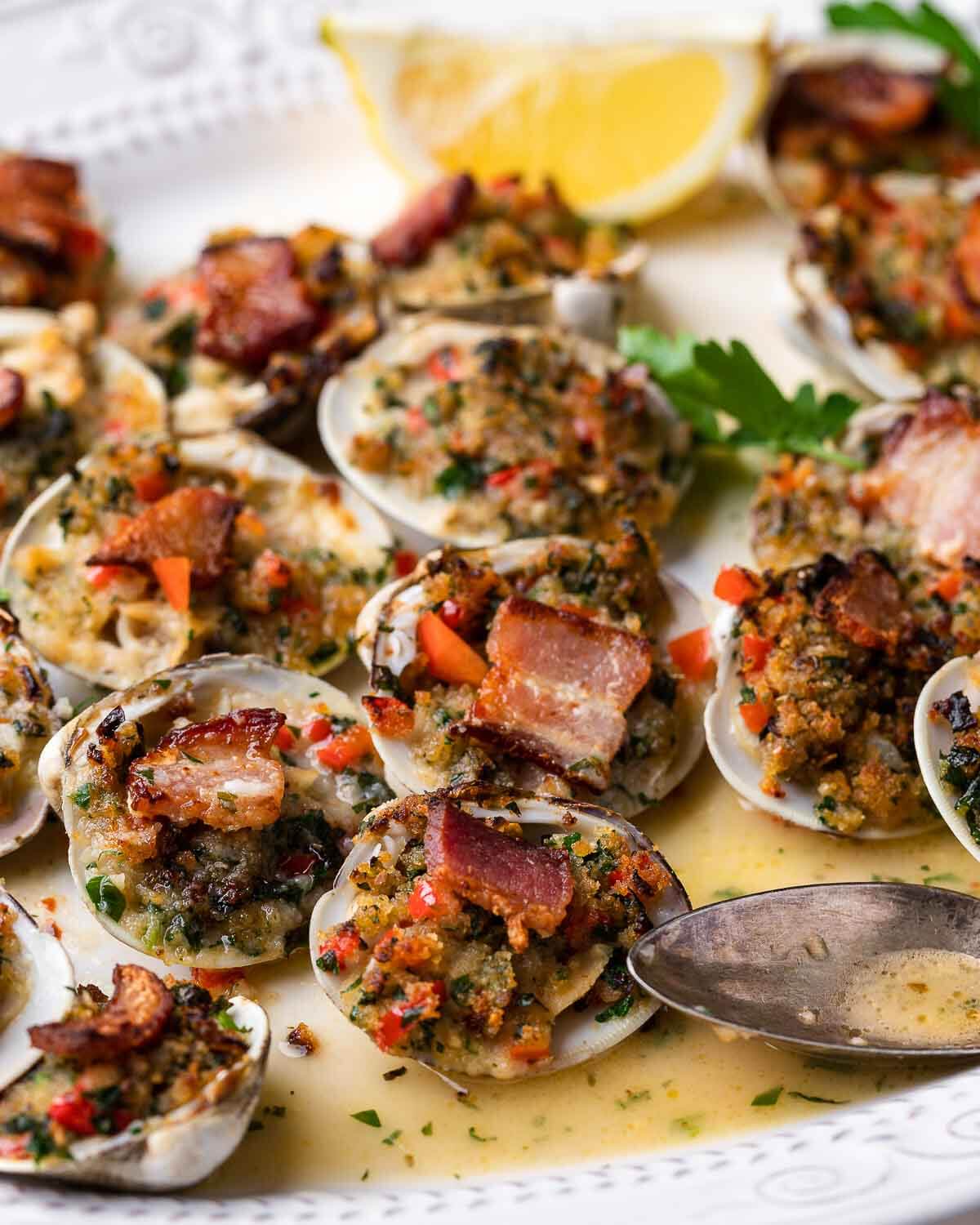 Clams casino in white plate with lemon wedges.