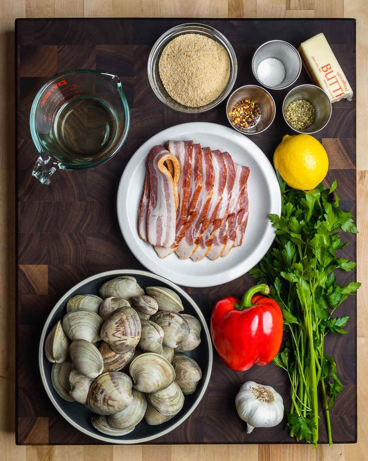 Ingredients shown: white wine, breadcrumbs, salt, chili flakes, oregano, butter, bacon, lemons, clams, bell pepper, garlic, and parsley.