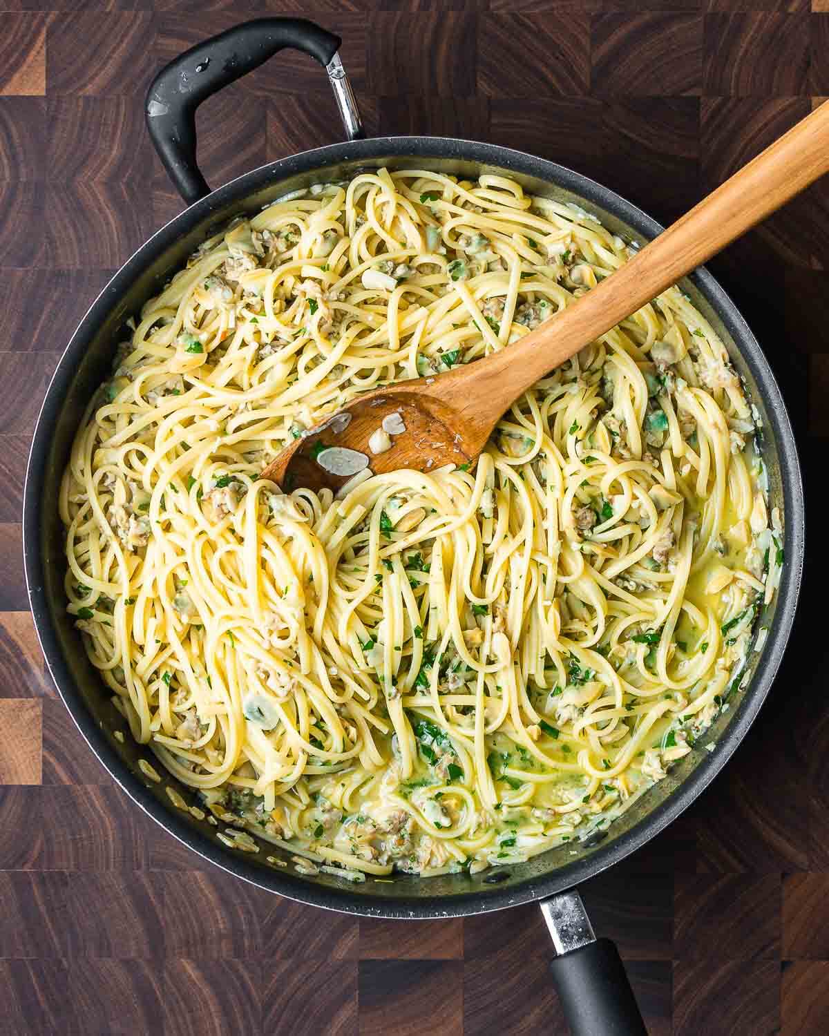 Overhead shot of Linguine with canned clam sauce in large black pan on cutting board.