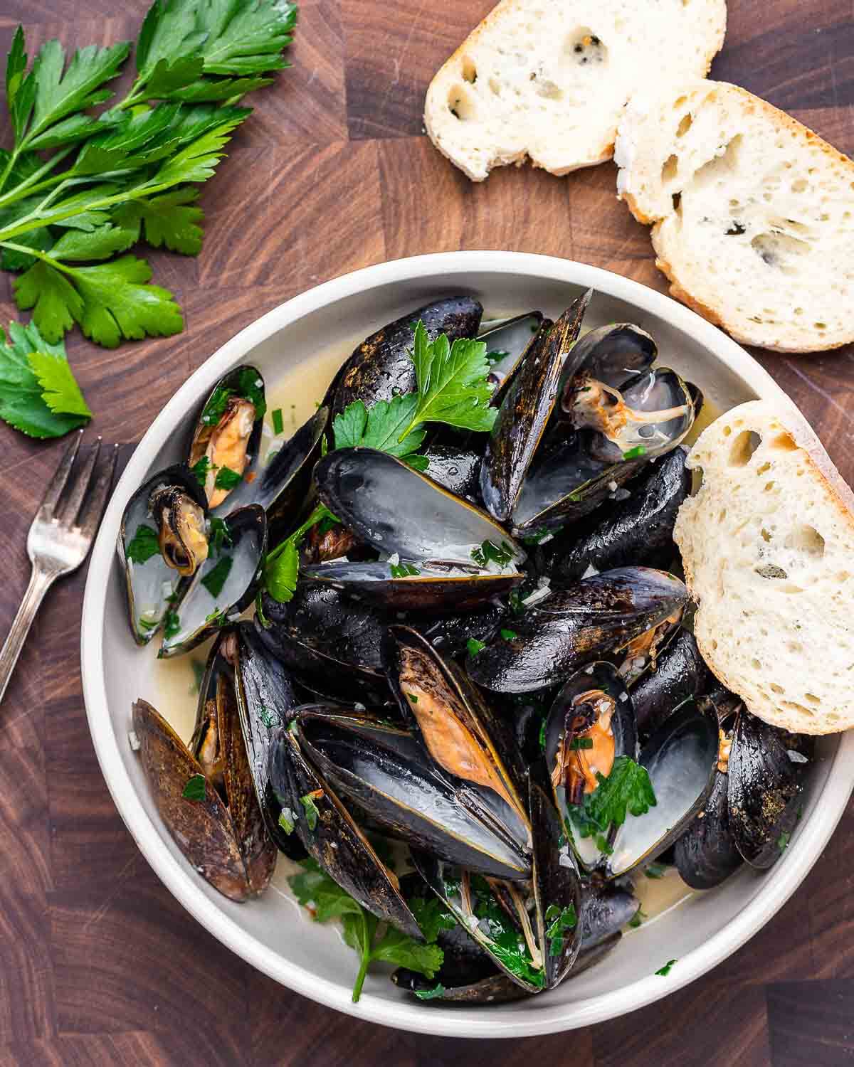 Overhead shot of steamed white wine mussels with slices of bread and parsley.