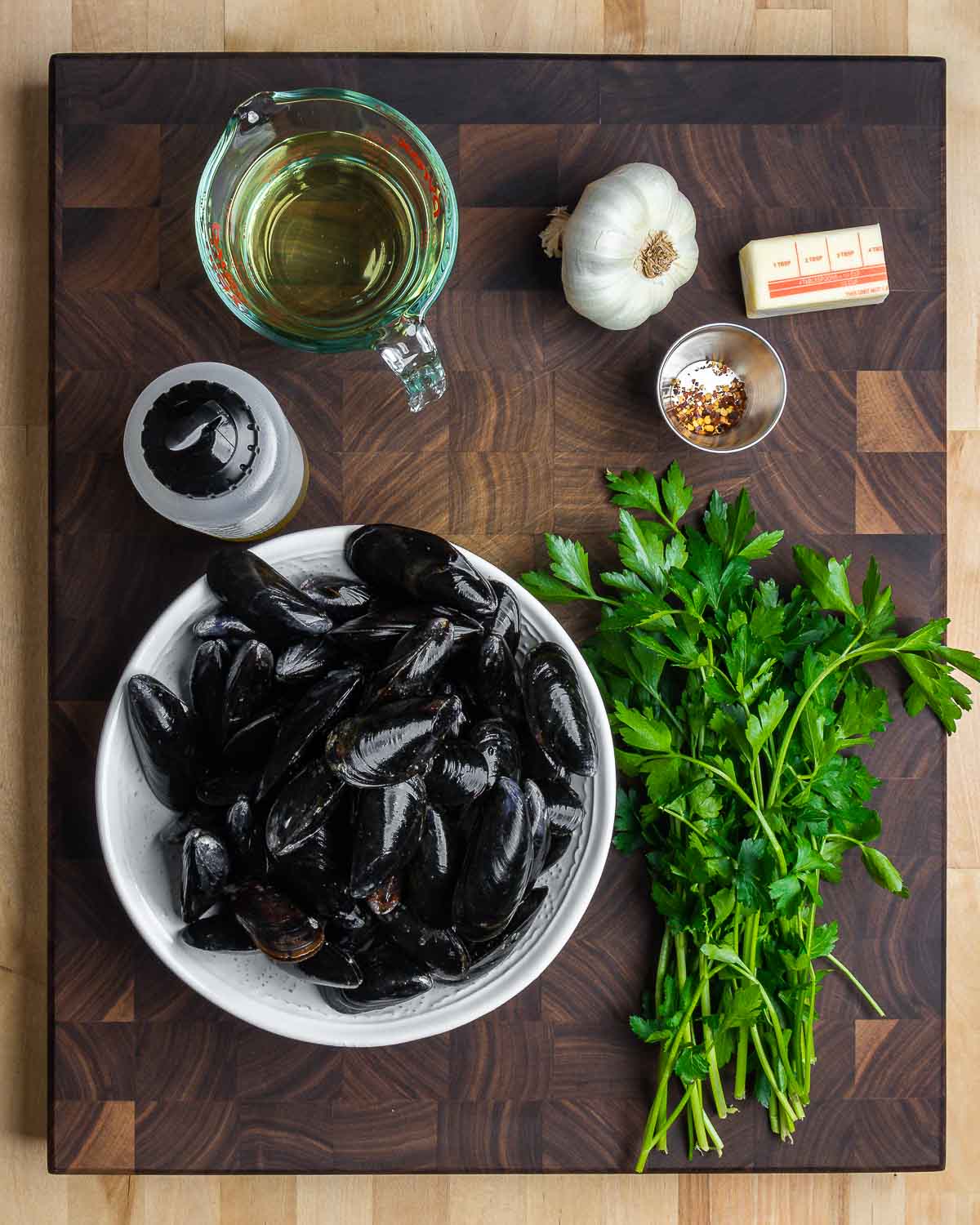 Ingredients shown: white wine, garlic, butter, olive oil, chili flakes, mussels, and parsley.