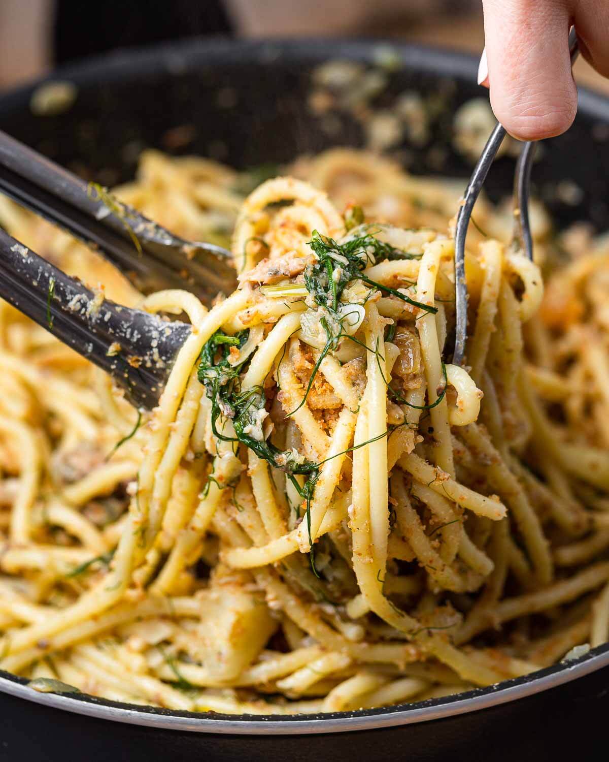 Hands tossing pasta con le sarde.