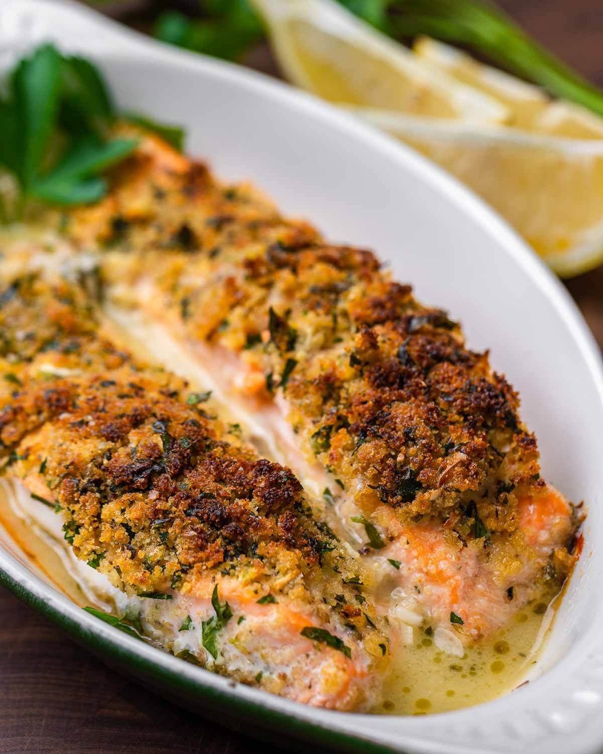 Small plate of salmon oreganata with lemons and parsley in the background.