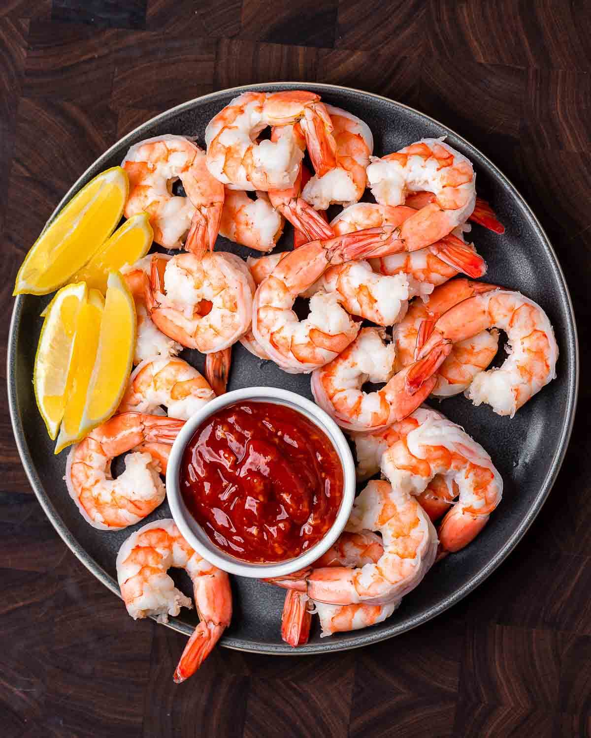 Overhead shot of large plate of shrimp cocktail with cocktail sauce and lemons.