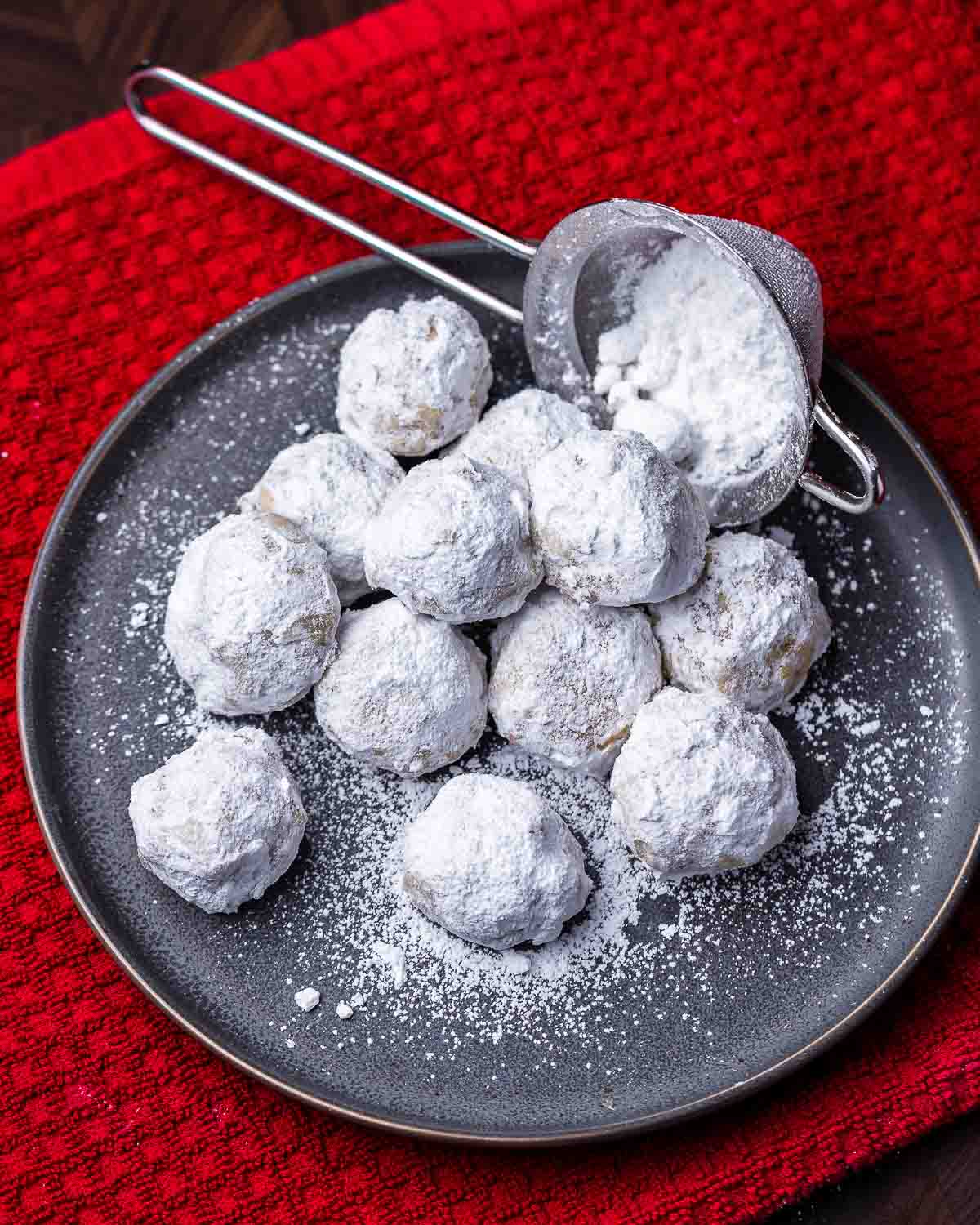 Plate of walnut snowball cookies on top of red towel.