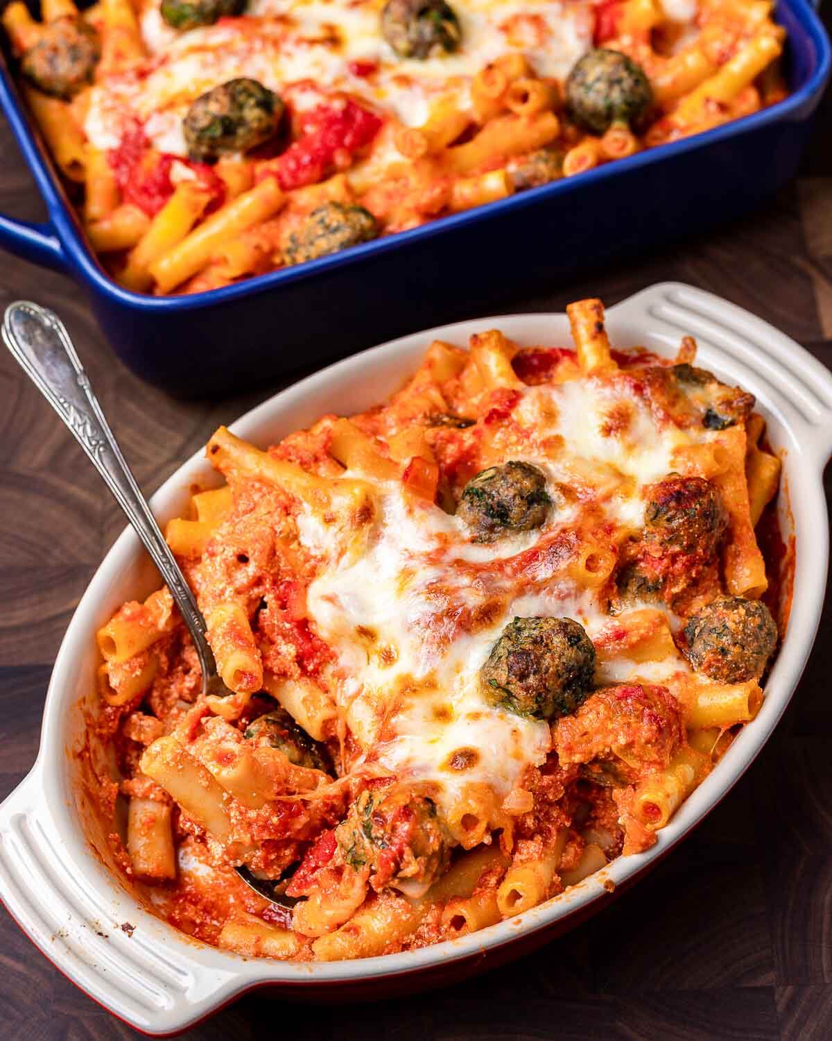 Baked ziti with meatballs in two baking dishes on walnut cutting board.