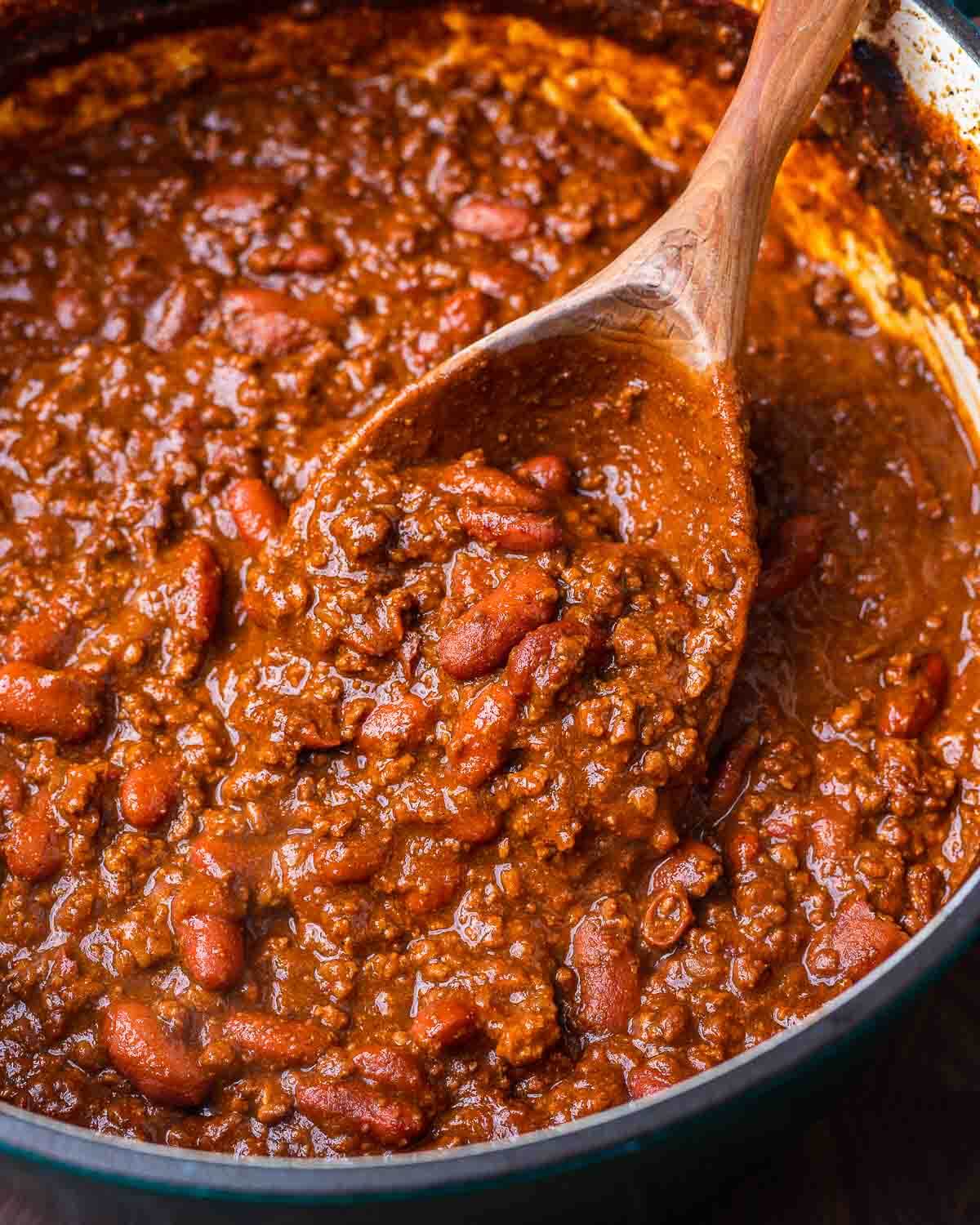 Large Dutch oven with classic chili and large wooden ladle.