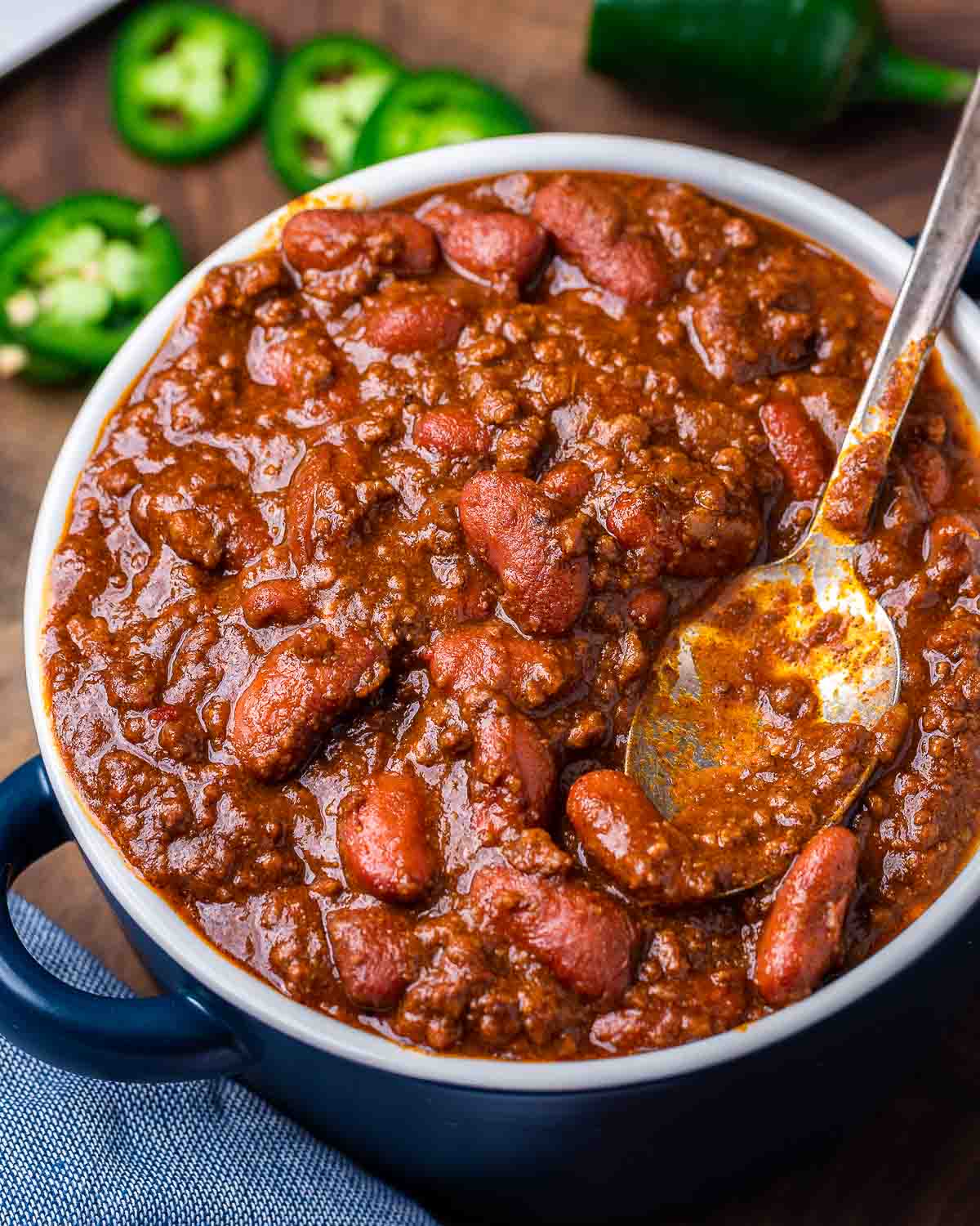 Large bowl of chili with jalapenos in the background.
