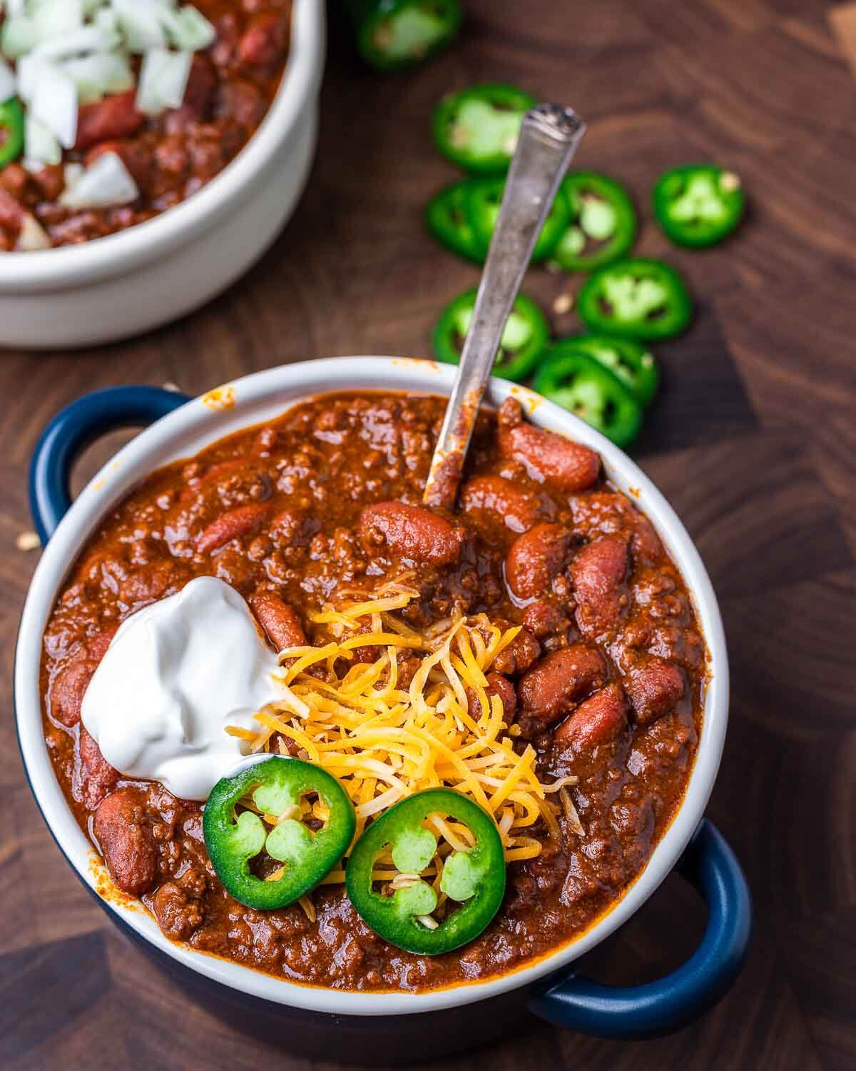 Bowl of chili topped with jalapeno, cheddar cheese, and sour cream.