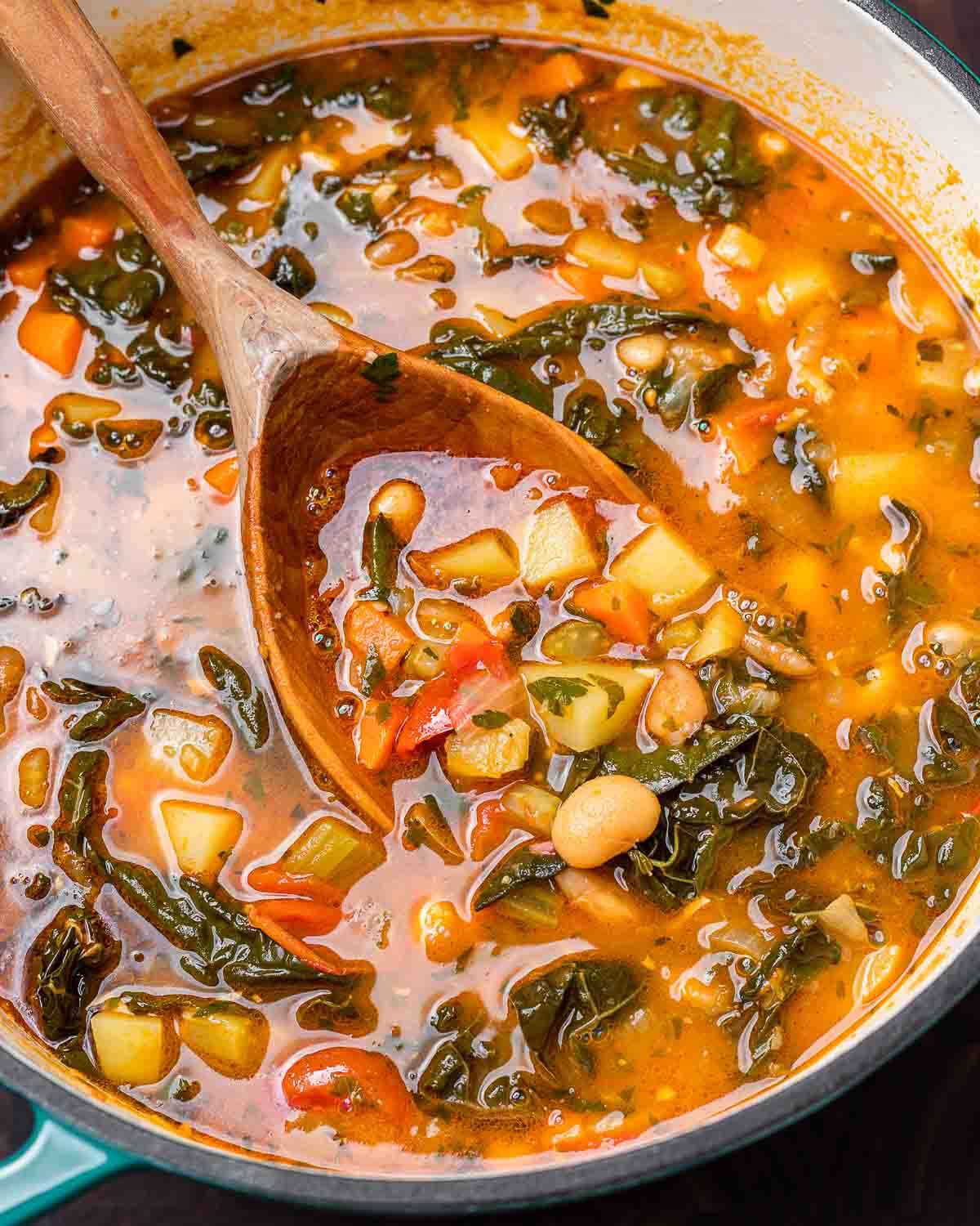 Large pot of minestrone soup with wooden ladle.