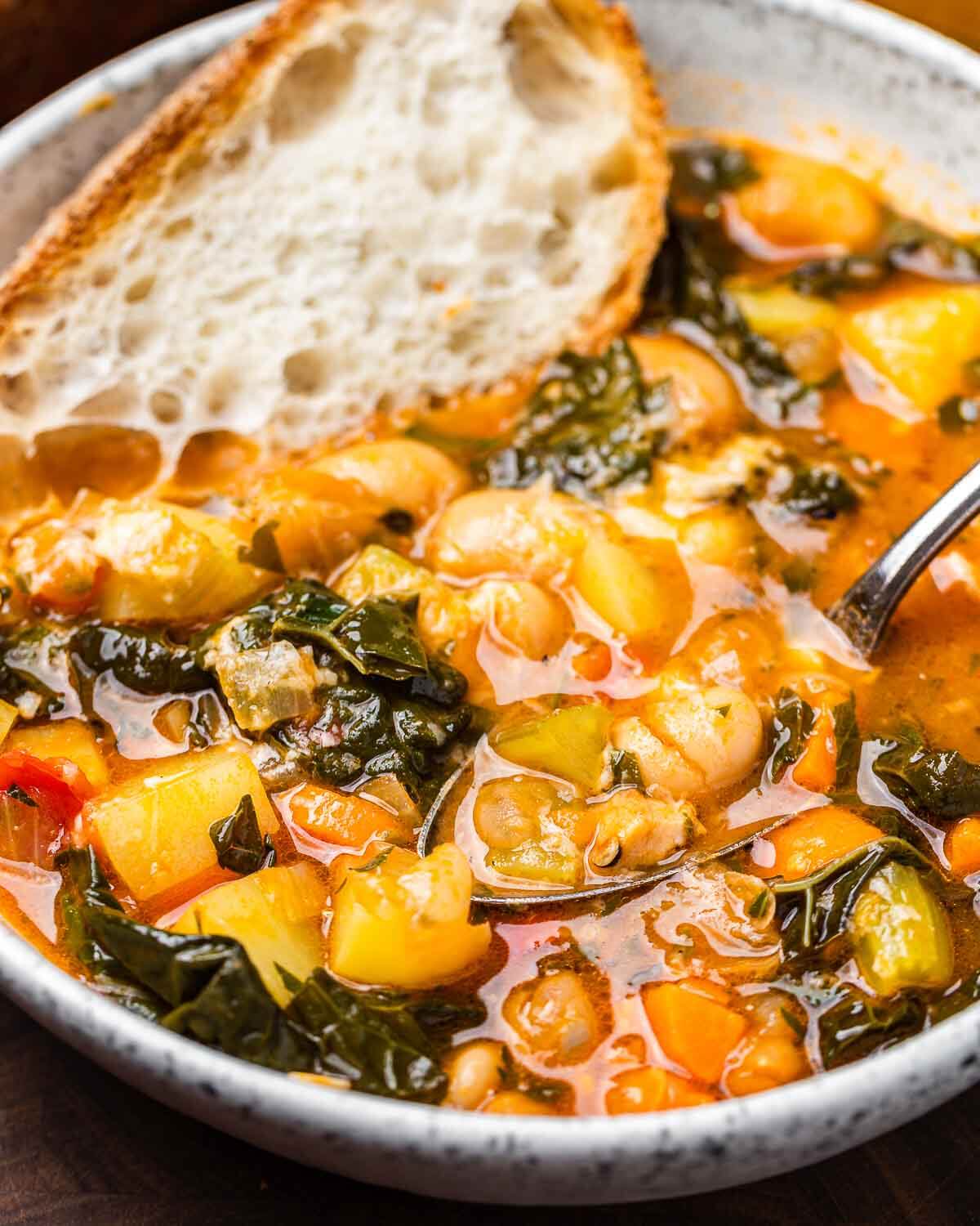 Large white bowl of minestrone soup with spoon and piece of bread.