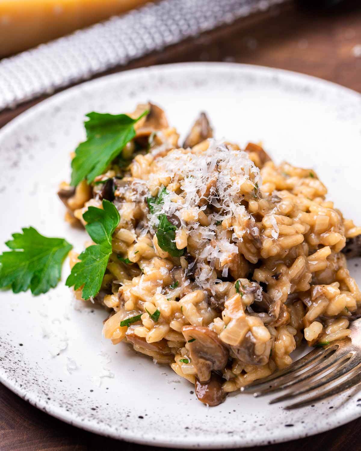 Mushroom risotto in white plate with shaved Parmigiano and parsley on top.