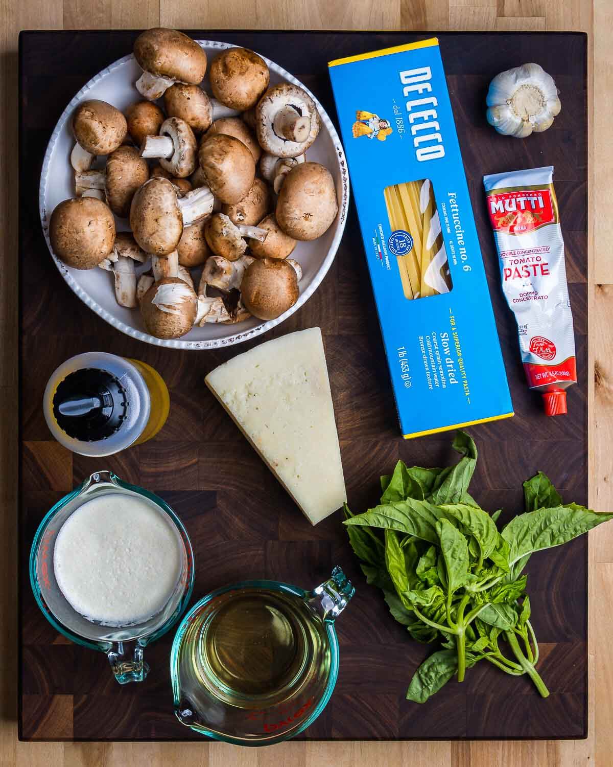 Ingredients shown: mushrooms, fettuccine, garlic, tomato paste, olive oil, Pecorino, heavy cream, white wine, and basil.