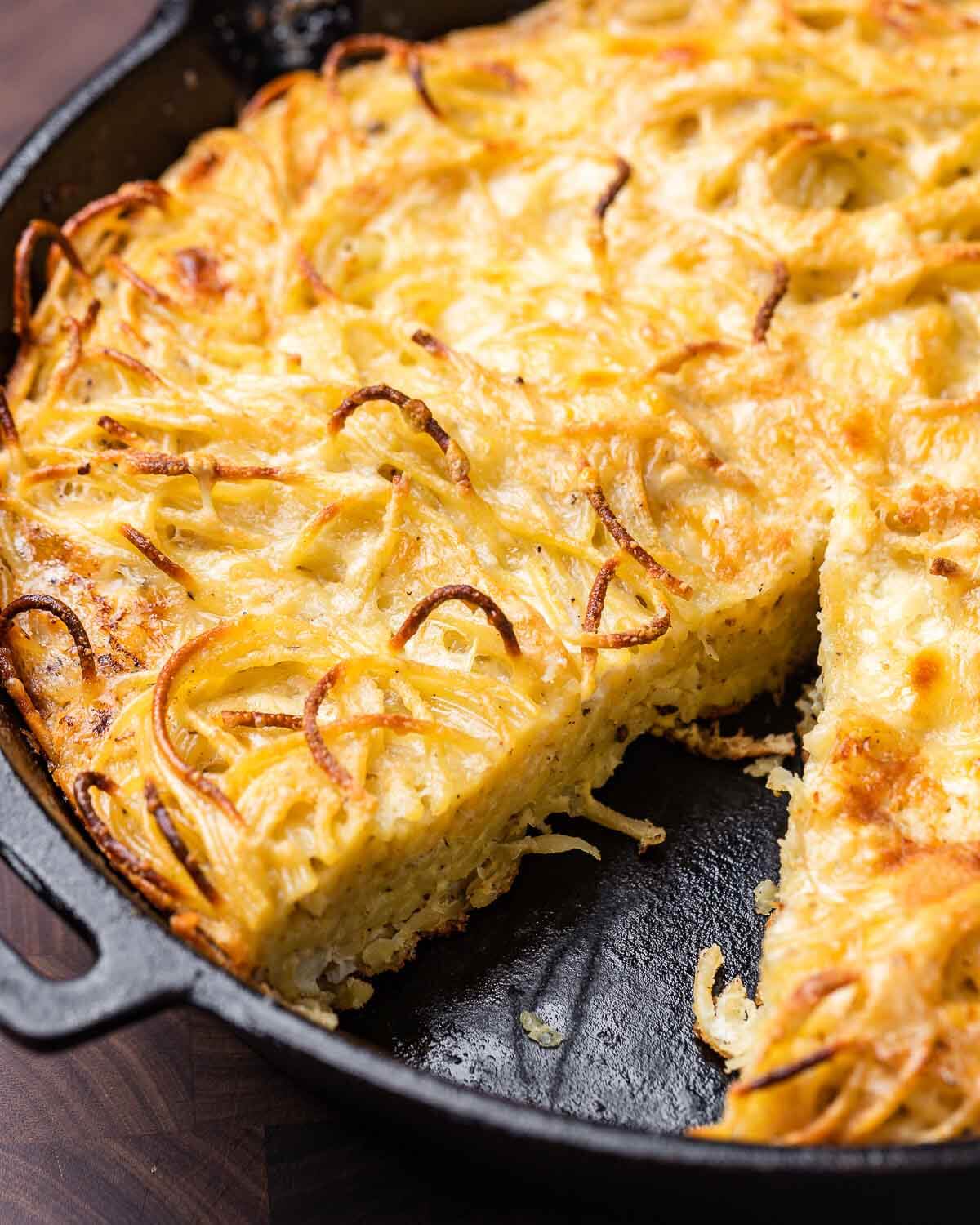 White spaghetti pie in cast iron pan with one slice missing.