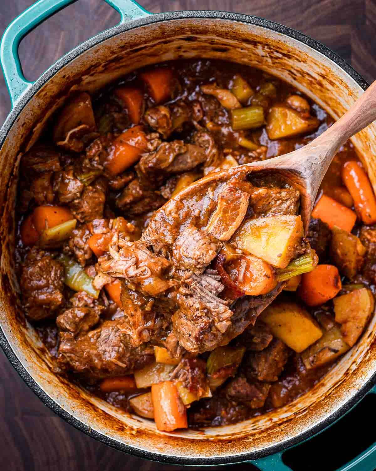 Overhead shot of Guinness beef stew in Dutch oven with wooden ladle.