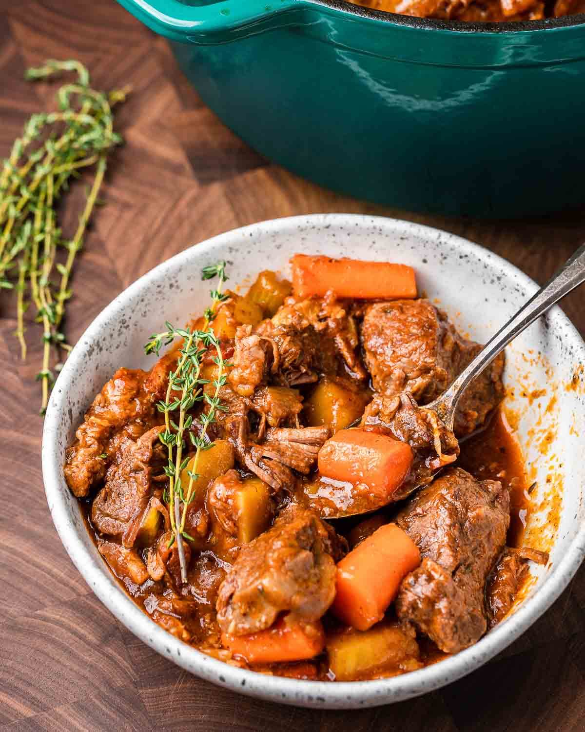 White bowl with Guinness beef stew along with blue Dutch oven pot in the background.