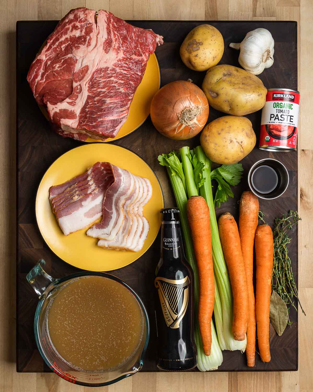 Ingredients shown: beef chuck, onion, potatoes, garlic, tomato paste, bacon, beef stock, Guinness, celery carrots, herbs, and Worcestershire sauce.
