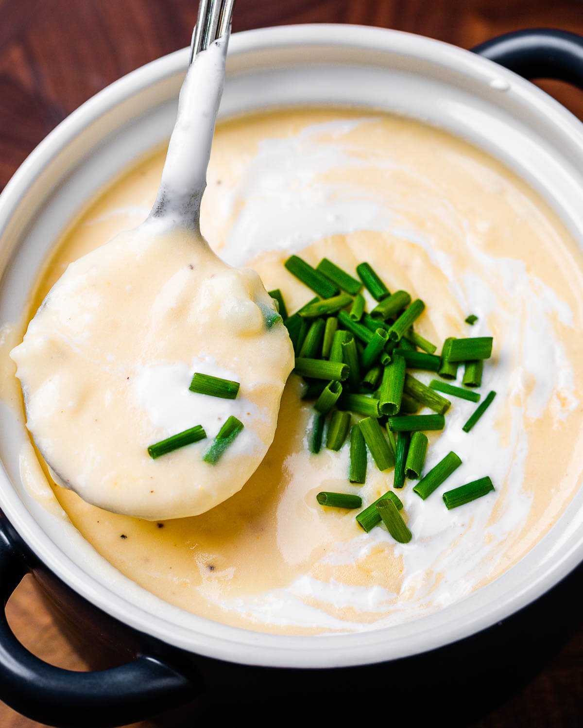 Spoon holding creamy baked potato soup over blue bowl.
