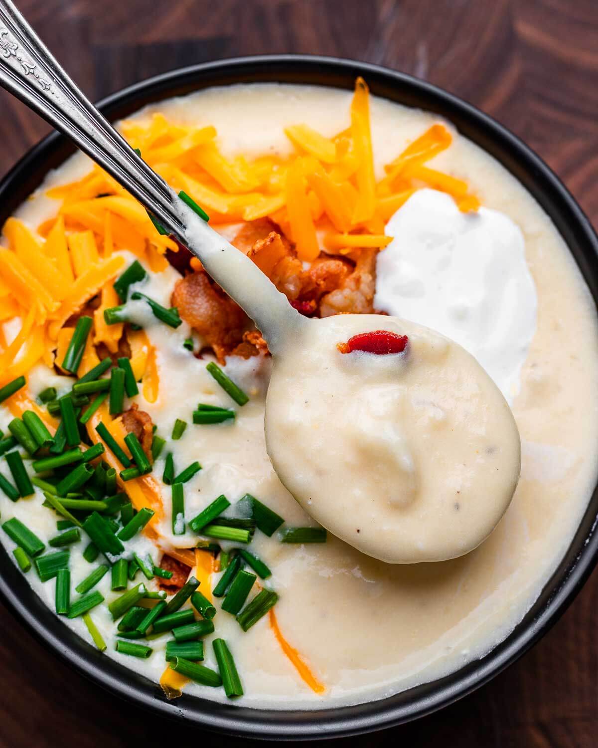 Black bowl of loaded baked potato soup.