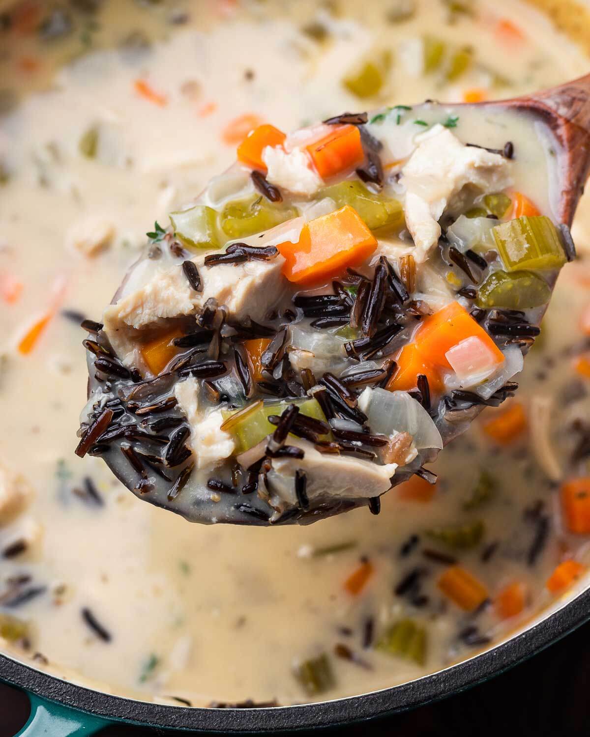 Large wooden ladle holding chicken wild rice soup over pot.