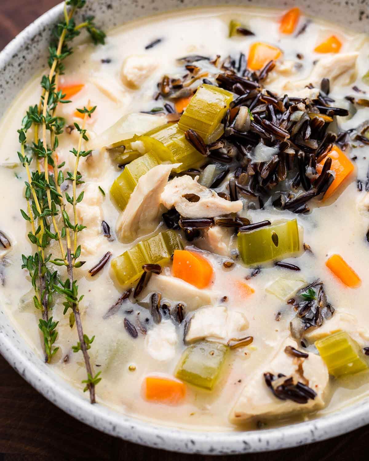 Overhead shot of white bowl with chicken wild rice soup and thyme garnish.