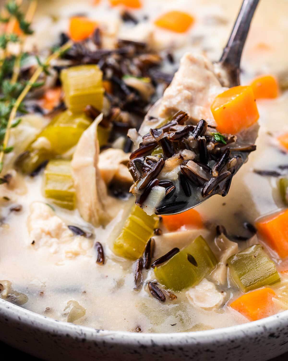 Spoonful of chicken wild rice soup held over white bowl.