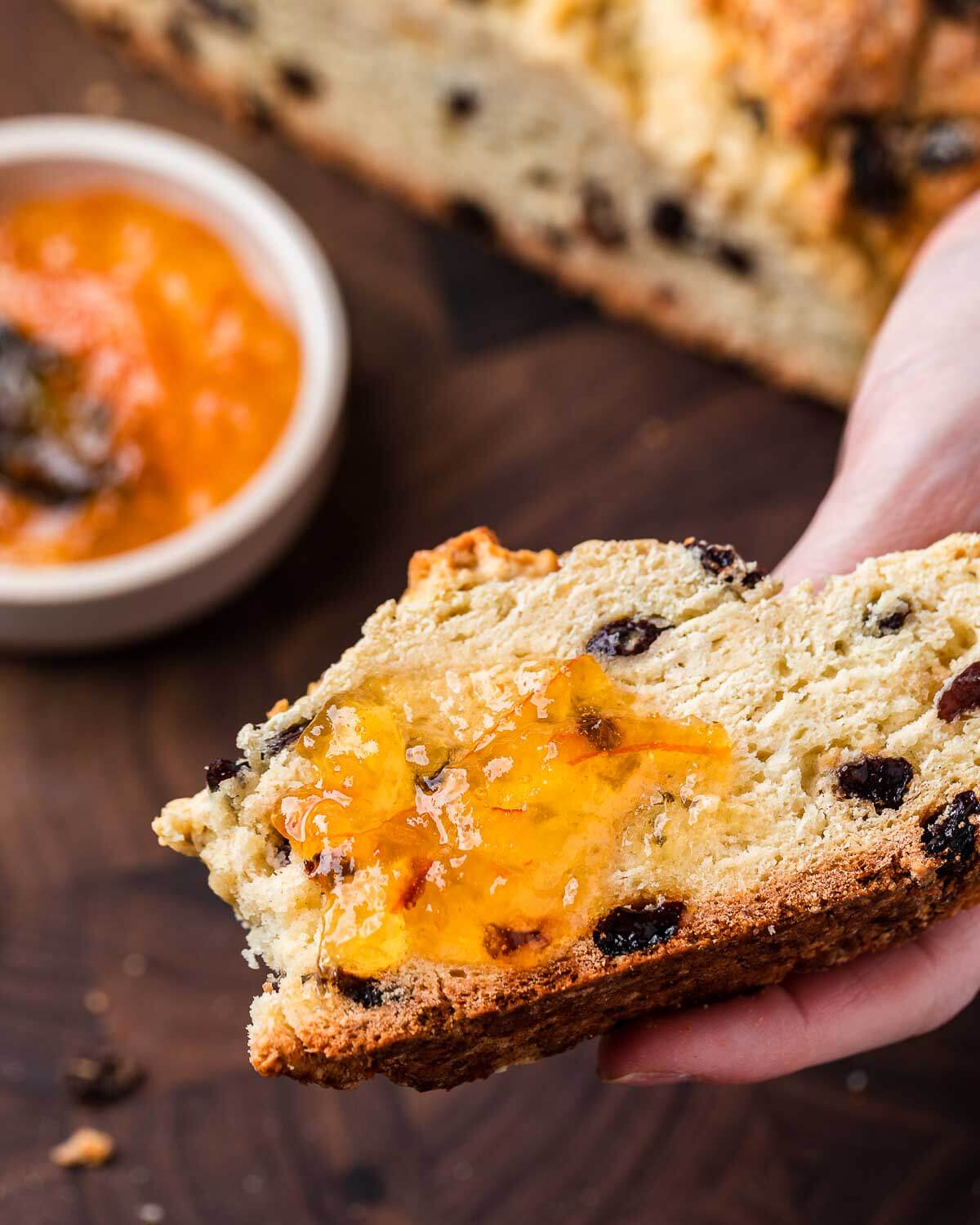 Hands holding slice of Irish soda bread with orange marmalade.