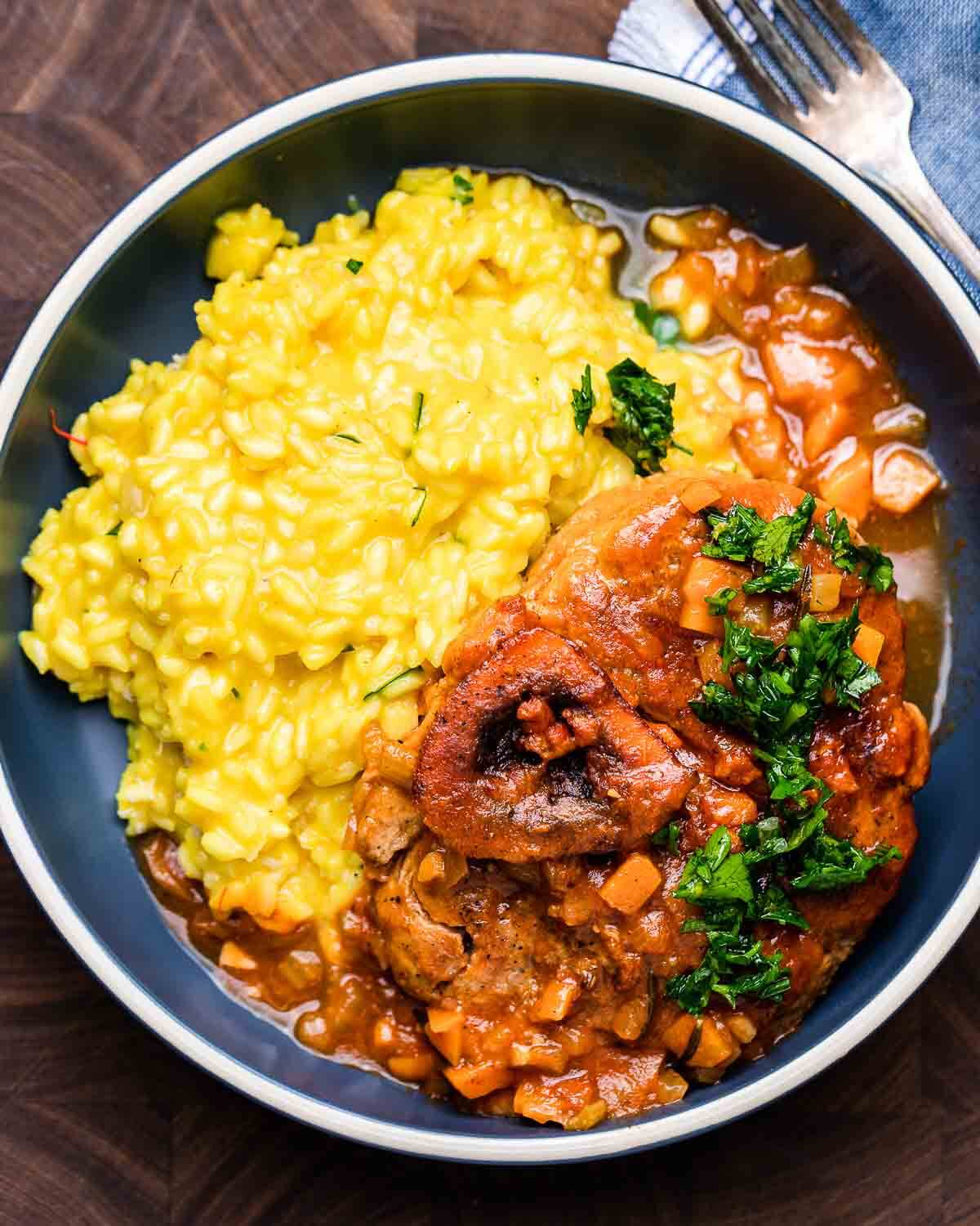 Ovehead shot of osso buco with risotto in blue plate.