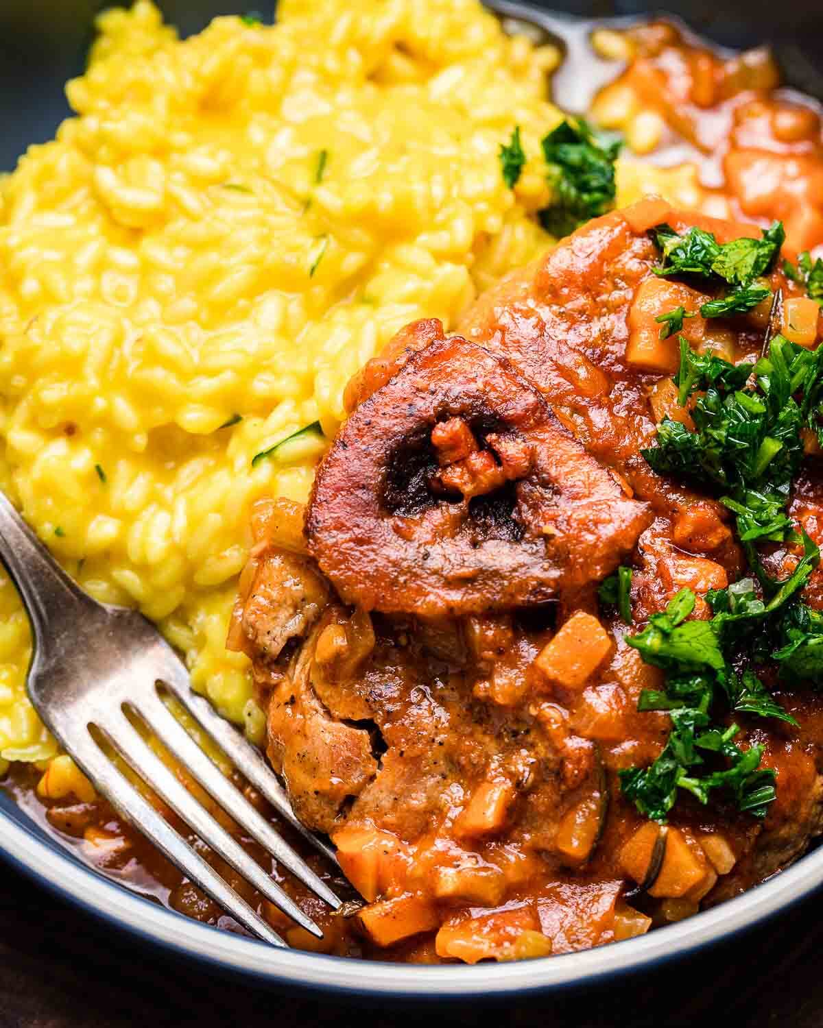 Closeup shot of osso buco with risotto topped with gremolata in blue plate.