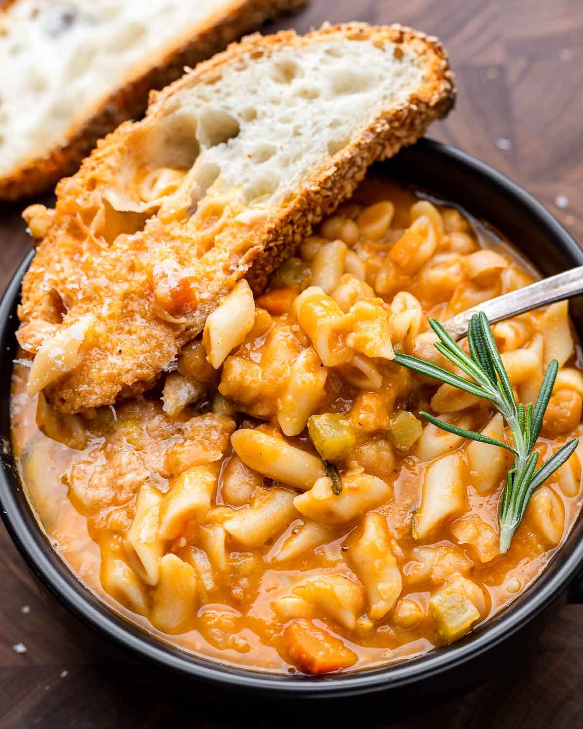 Overhead shot of black bowl with pasta e ceci and piece of bread.