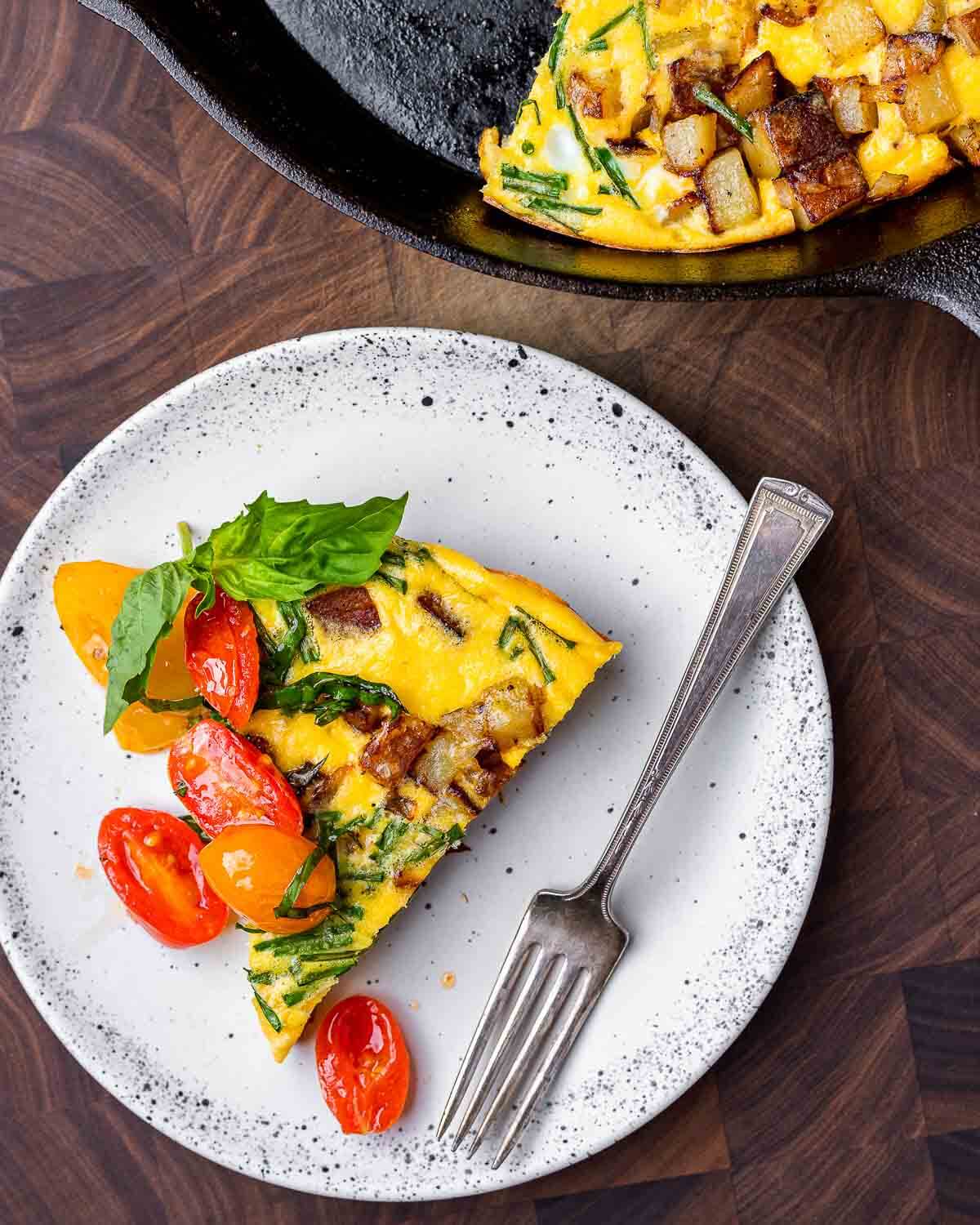 Overhead shot of slice of potato frittata with cherry tomato topping in white plate.